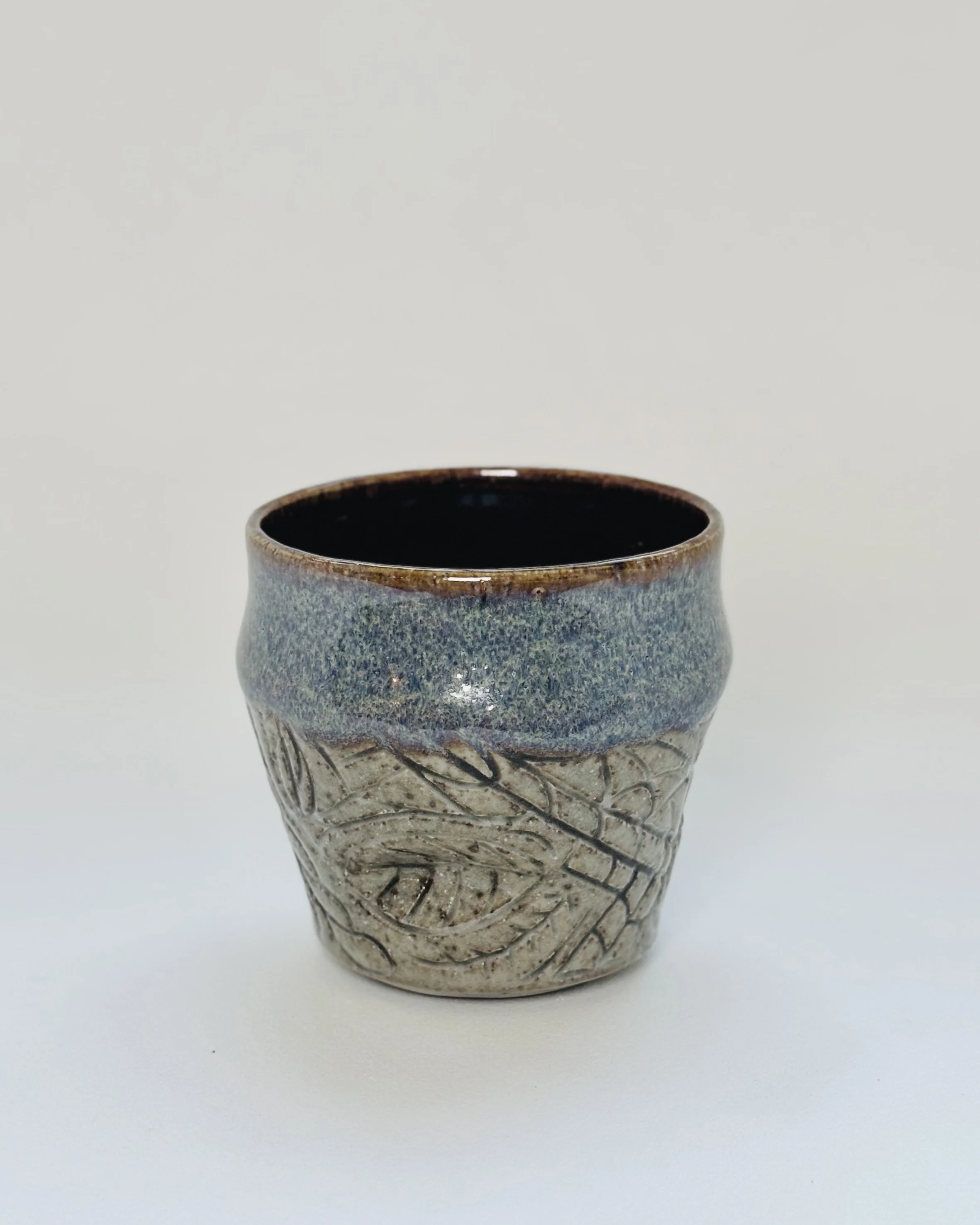 A small, ceramic cup with a textured, artistic design on a plain white background.