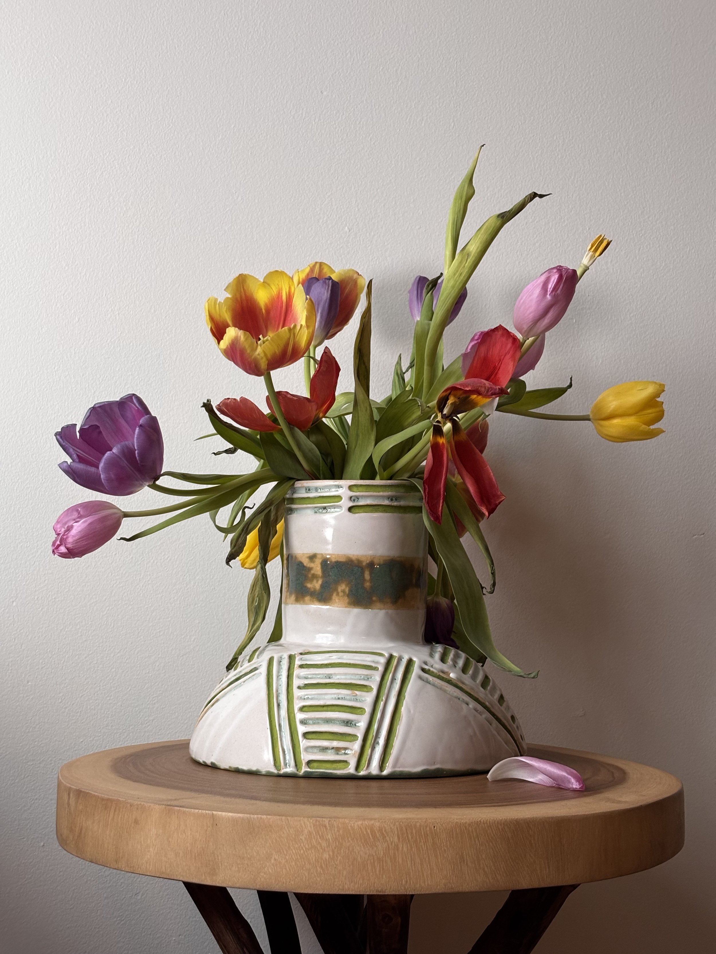 Colorful tulips in a ceramic vase on a wooden table against a plain wall.