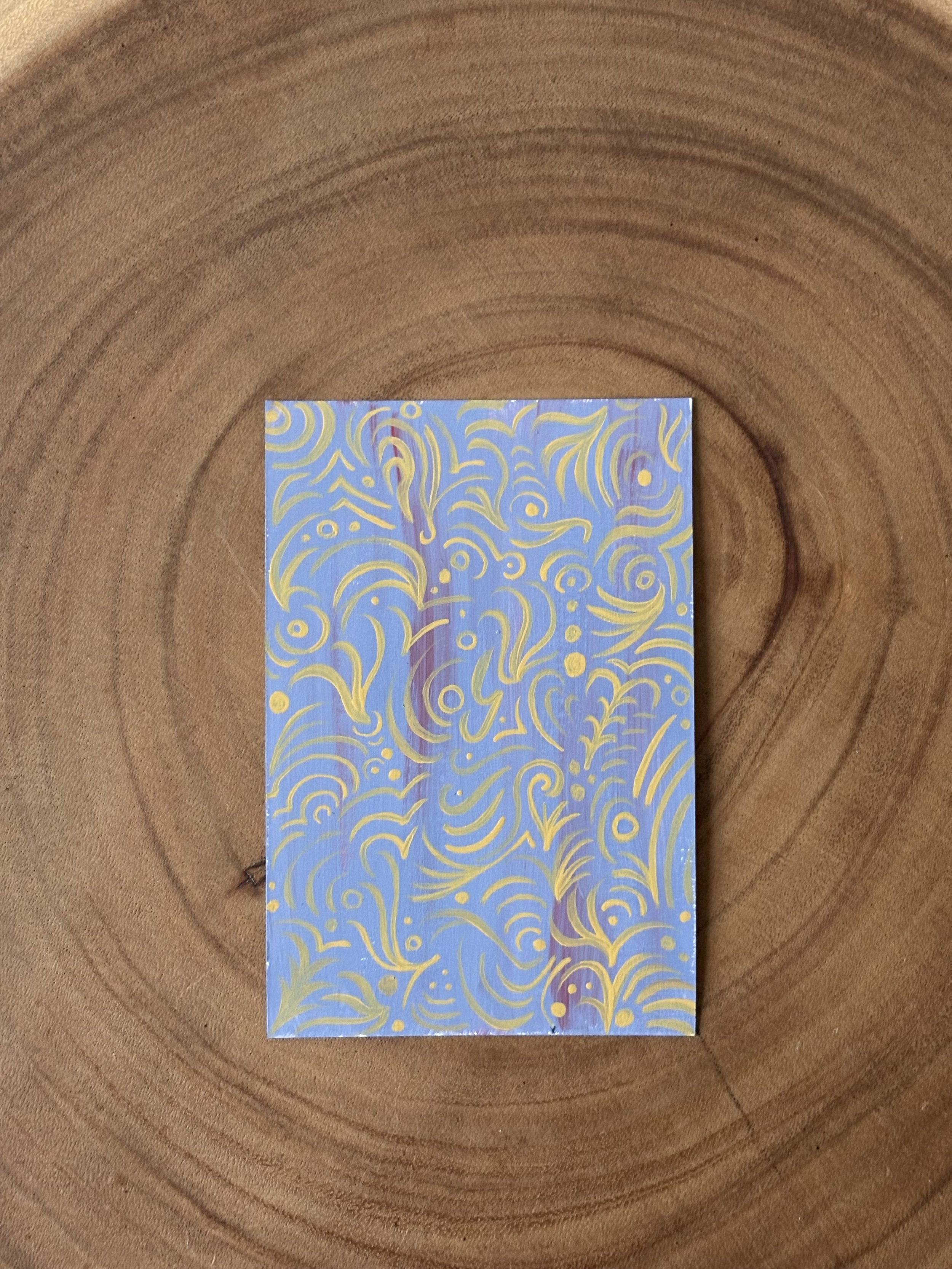 A small rectangular card with an abstract swirling pattern in shades of purple, blue, and yellow, placed on a wooden surface.