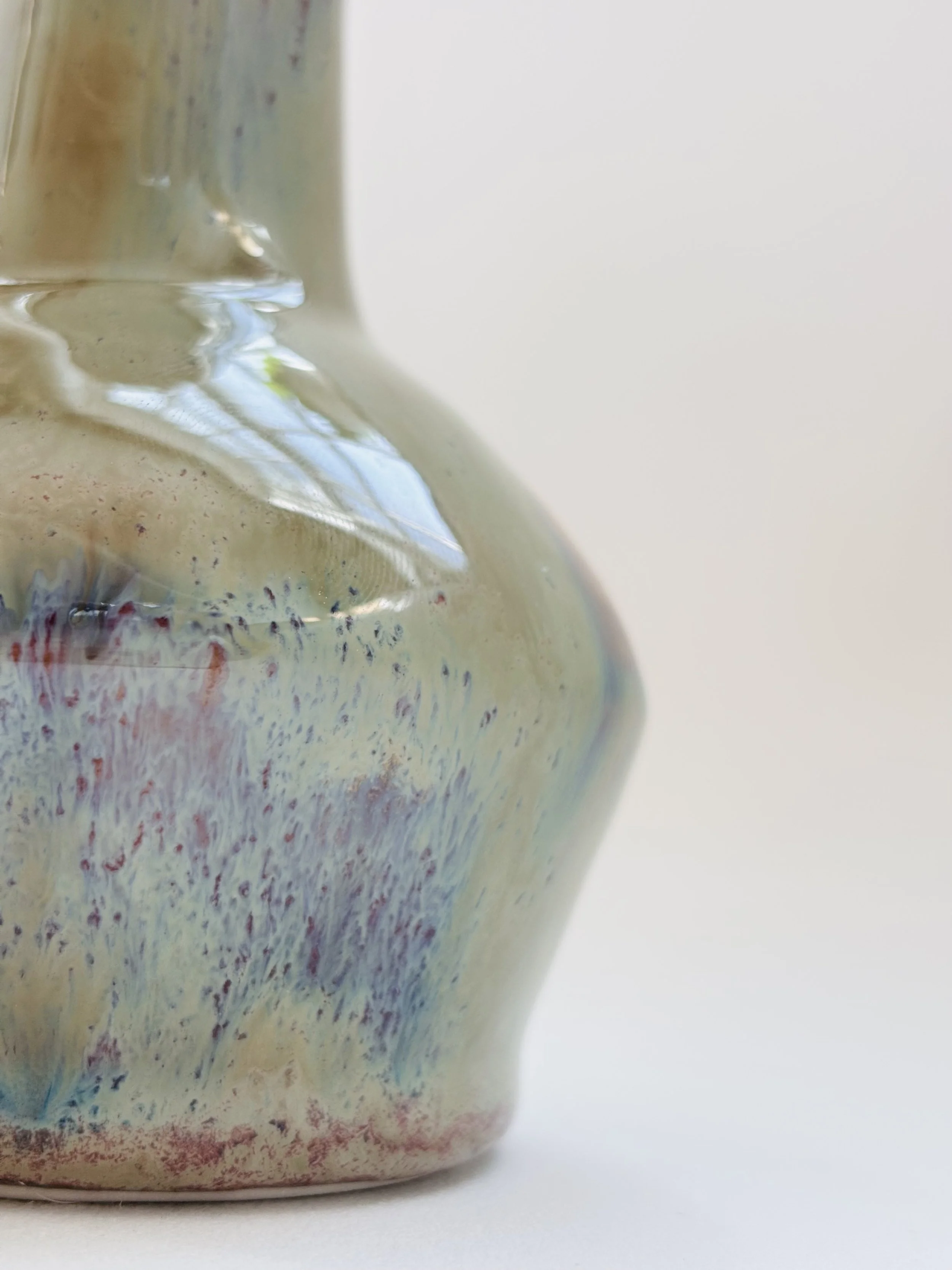 Close-up of a ceramic bottle with a iridescent finish, against a plain light background.