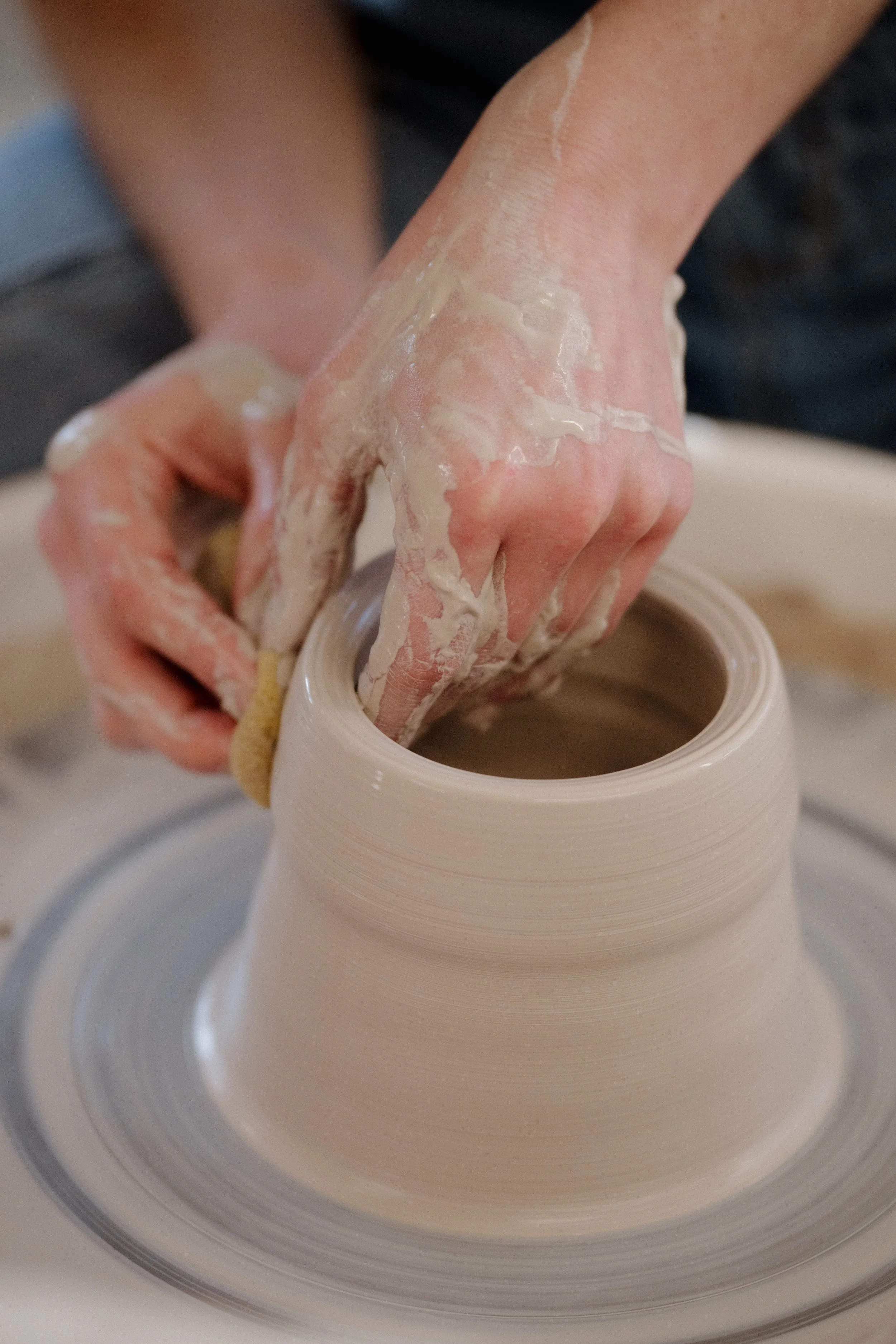 Hands shaping a clay vase on a pottery wheel in a pottery studio.