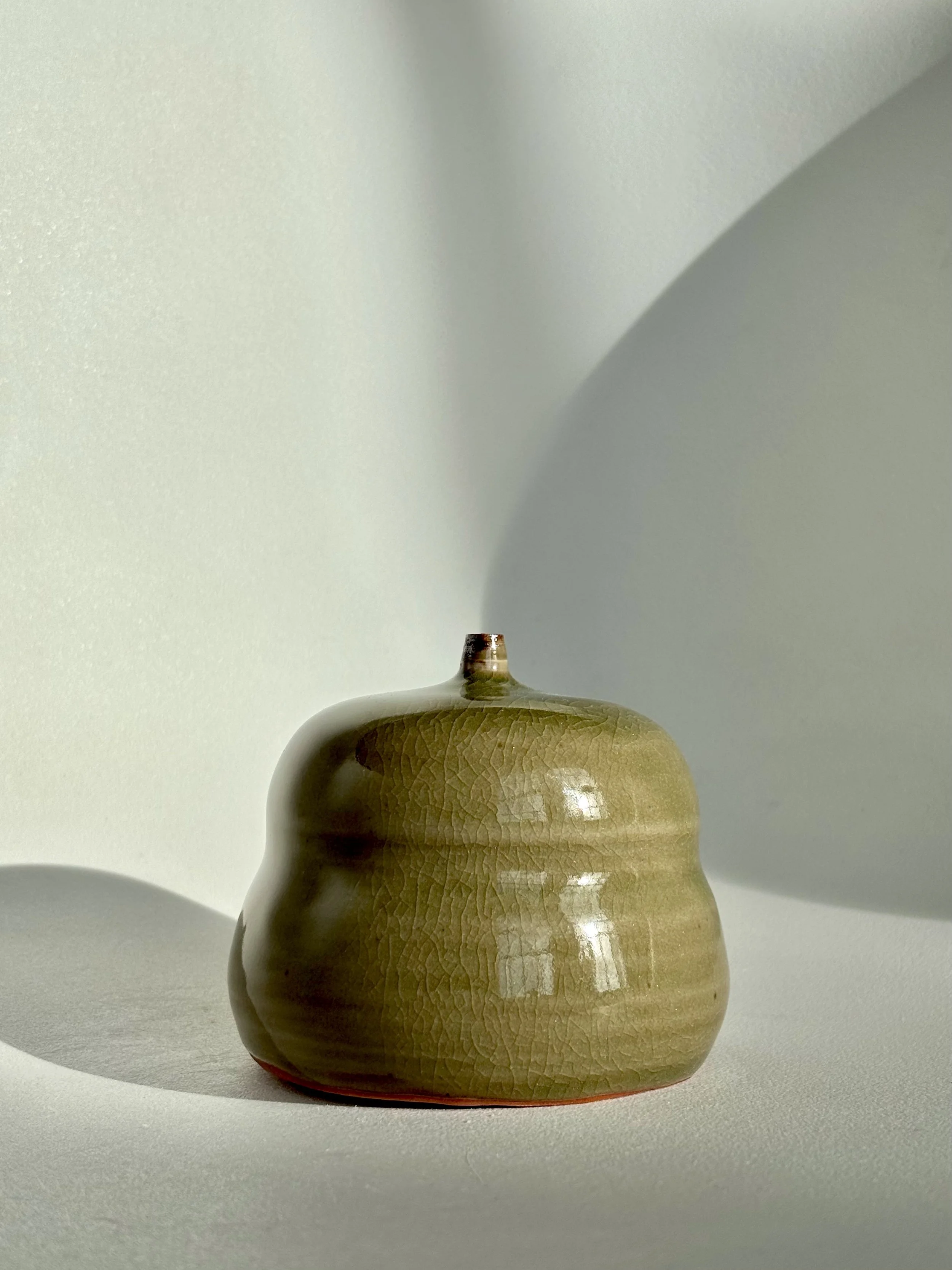 A brown ceramic vase with a rounded shape and textured surface, casting a shadow on a white background.