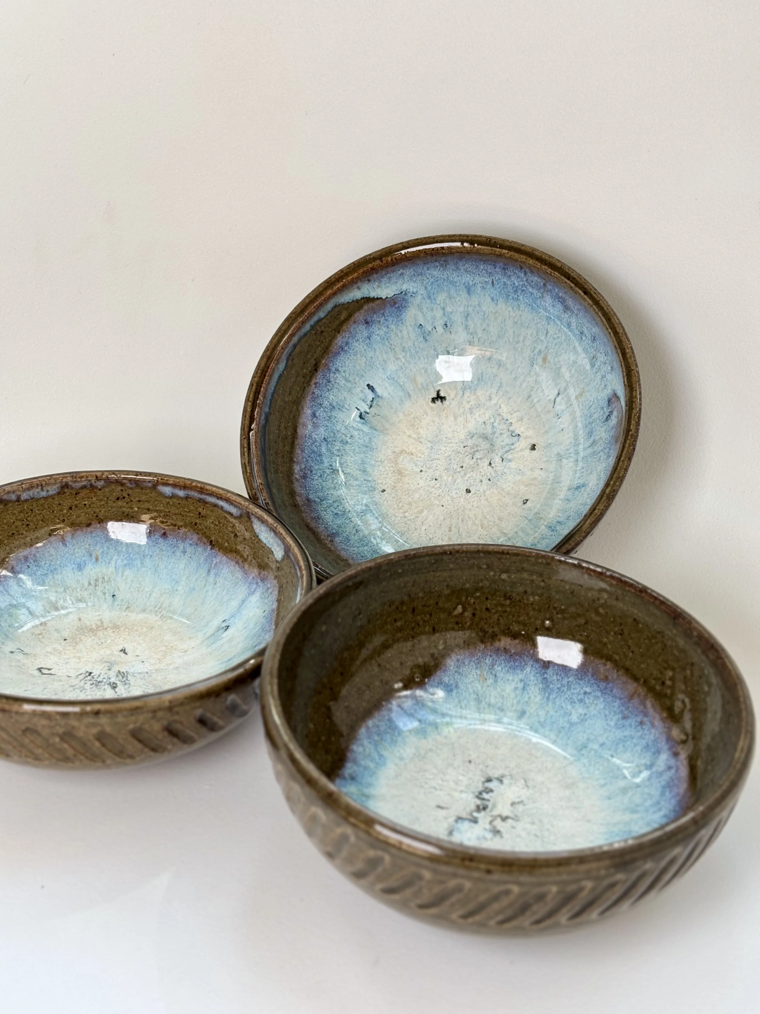 Three small ceramic bowls with blue and brown glaze, arranged on a white surface.