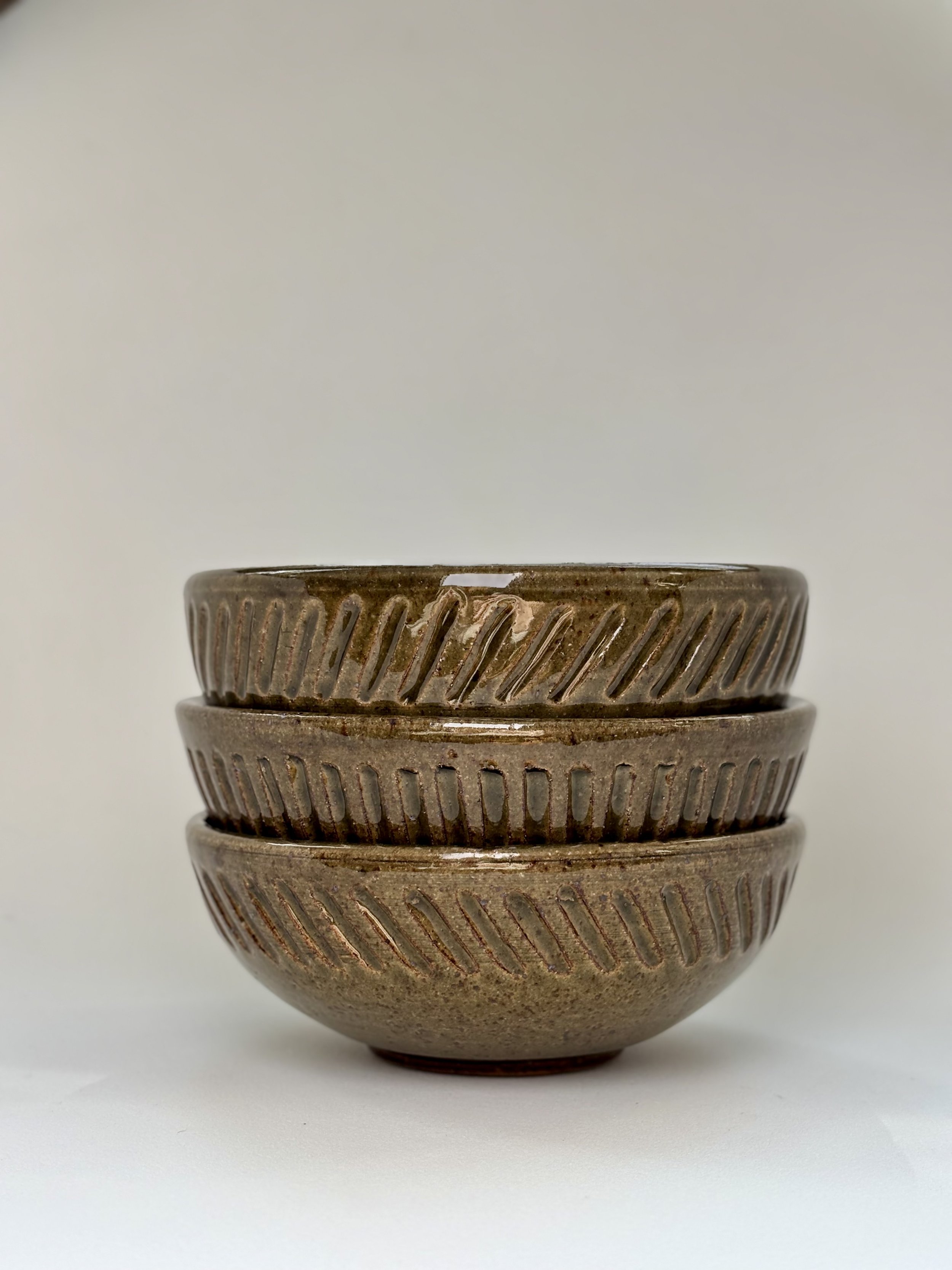 Three stacked brown ceramic bowls with diagonal striped patterns on their outer surfaces against a plain light background.