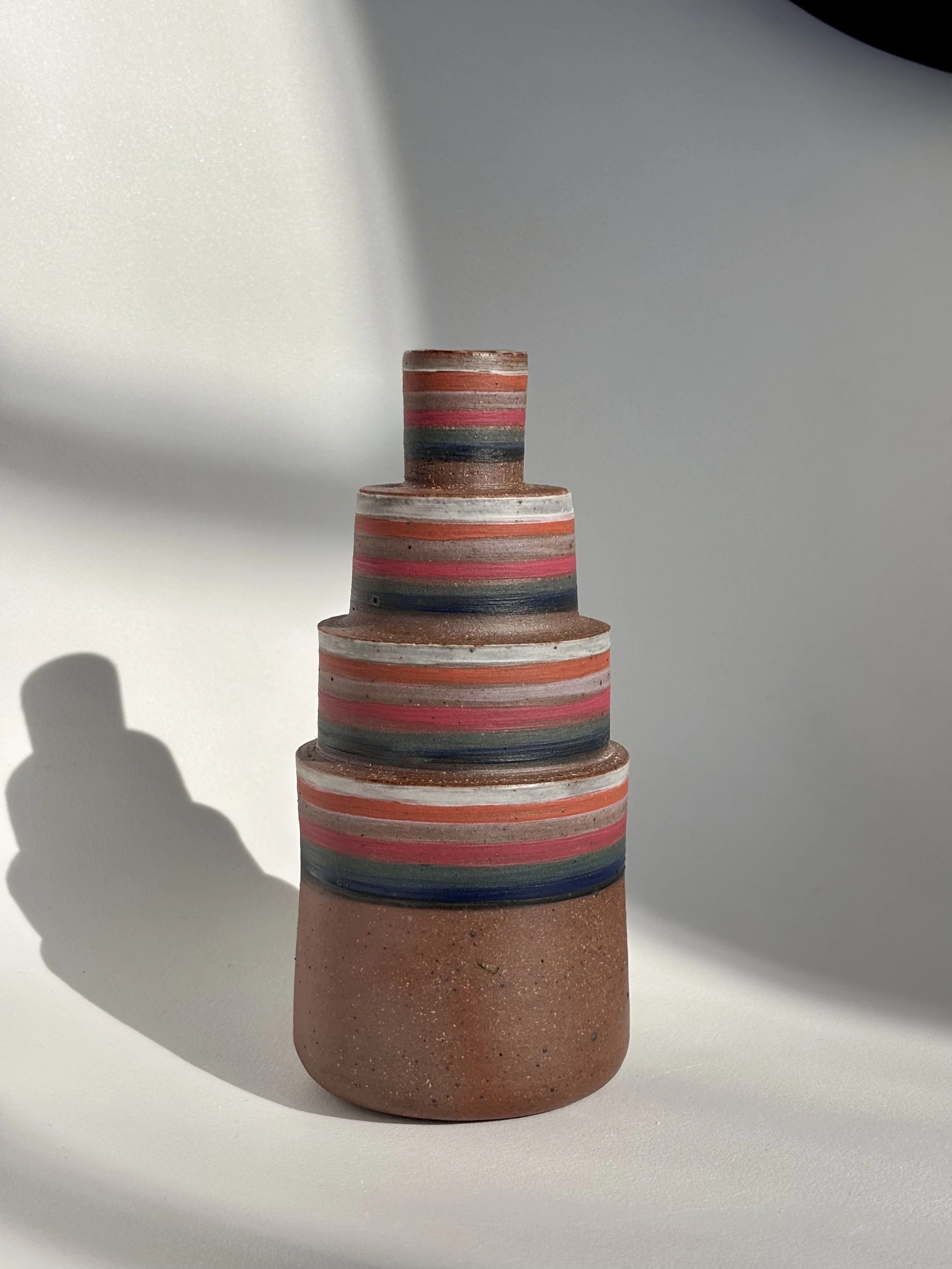 Colorful ceramic vase with horizontal stripes, placed on a white surface with a shadow cast to the left.