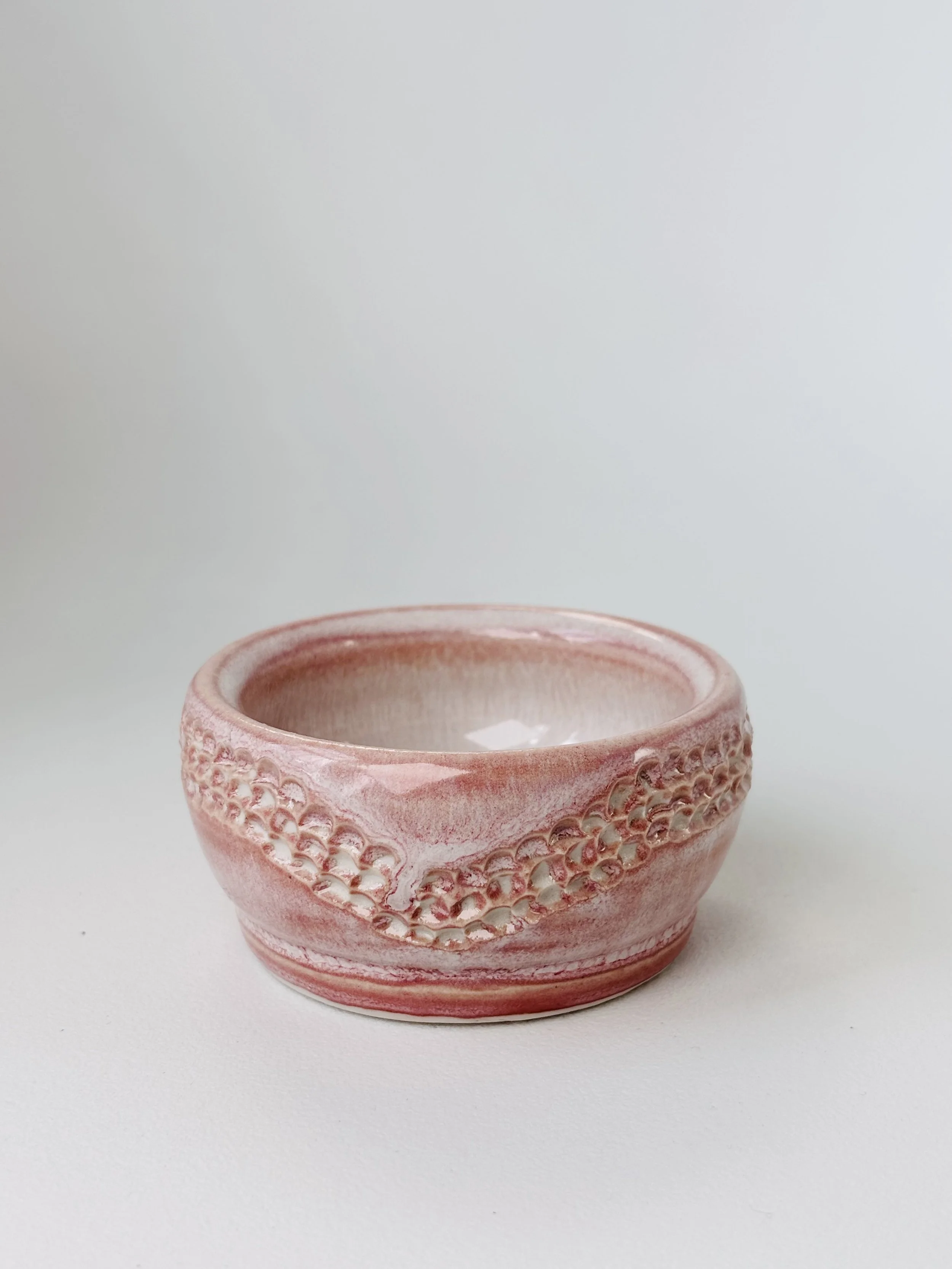 Pink ceramic bowl with textured decorative pattern, on a white surface.
