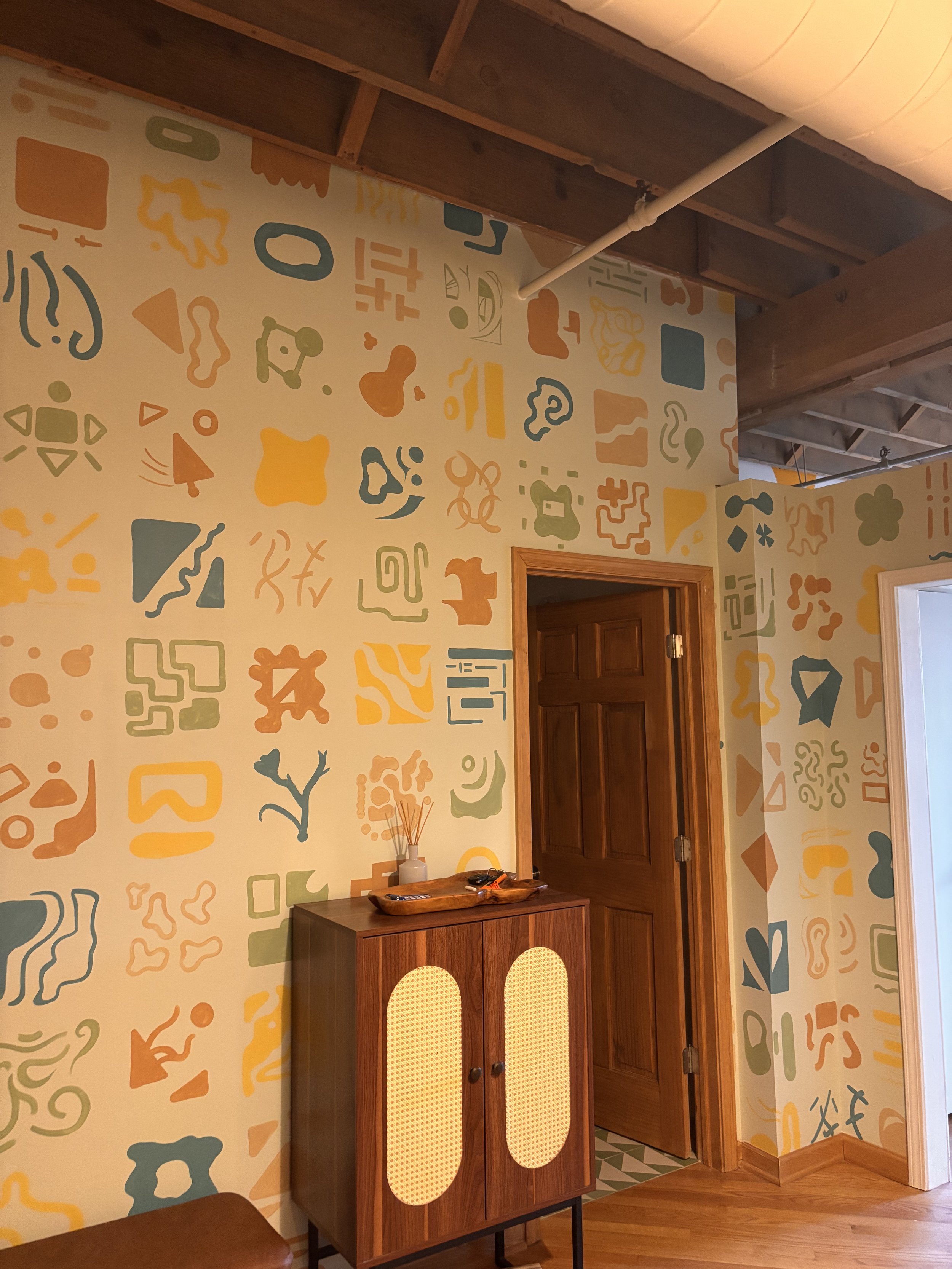 Decorative mural wall with colorful abstract patterns, wooden door, and wooden cabinet in a cozy room. Residential mural.