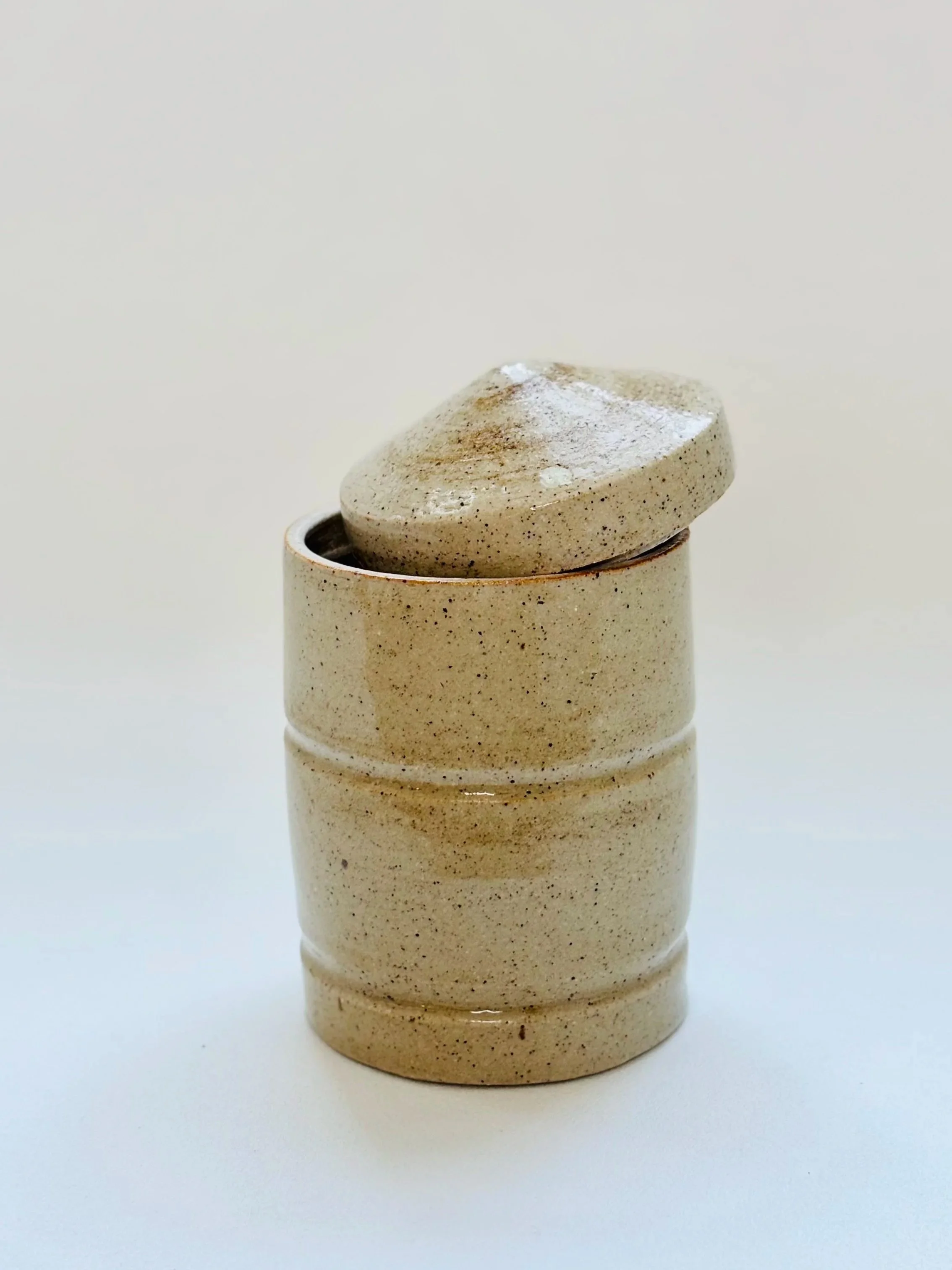 A beige ceramic container with a lid, set against a plain white background.