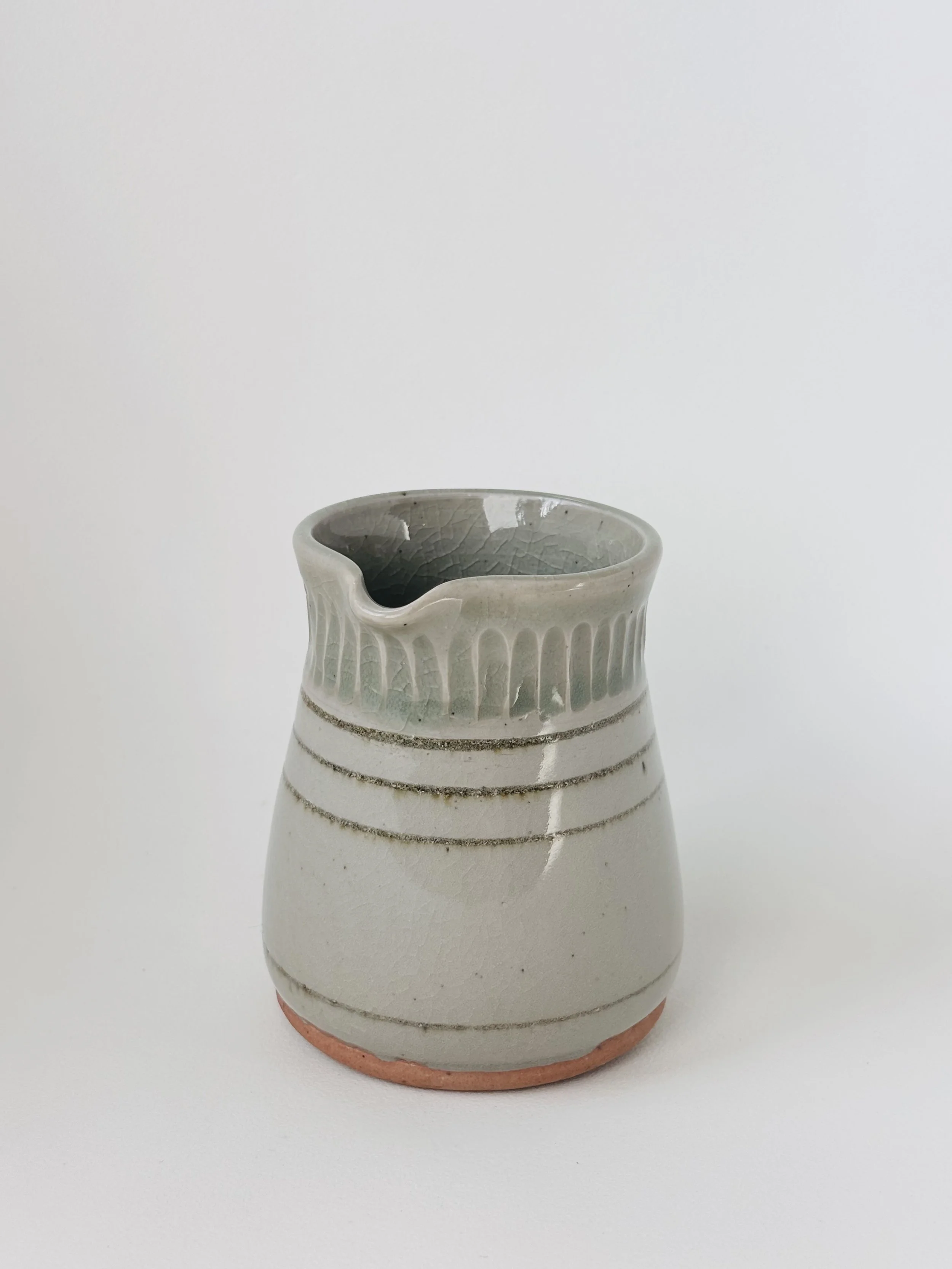 White ceramic creamer with horizontal textured lines and a small spout, placed on a white background.