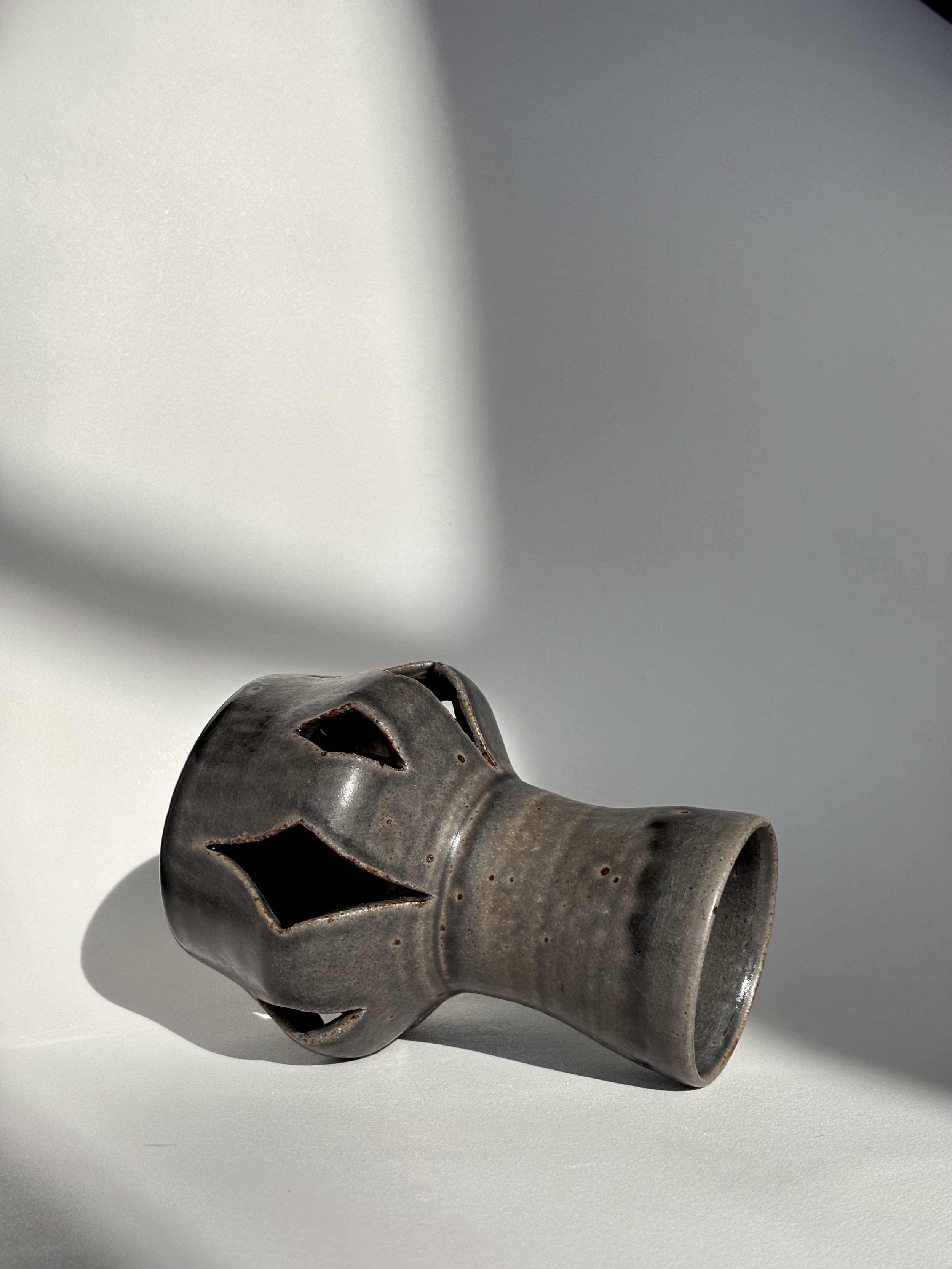 A ceramic vase, lying on its side on a white surface with shadows and a simple background.