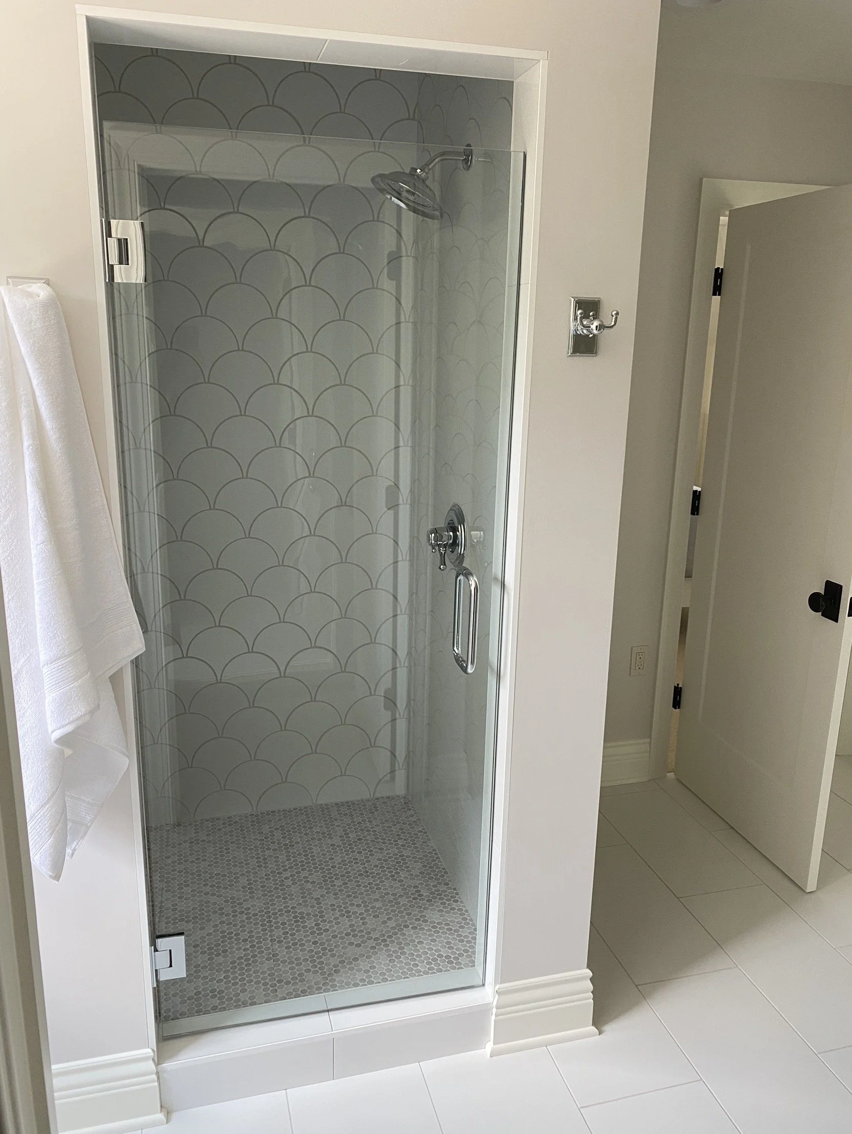 A glass shower enclosure with a patterned tile wall and floorto ceiling tile work in a bathroom.