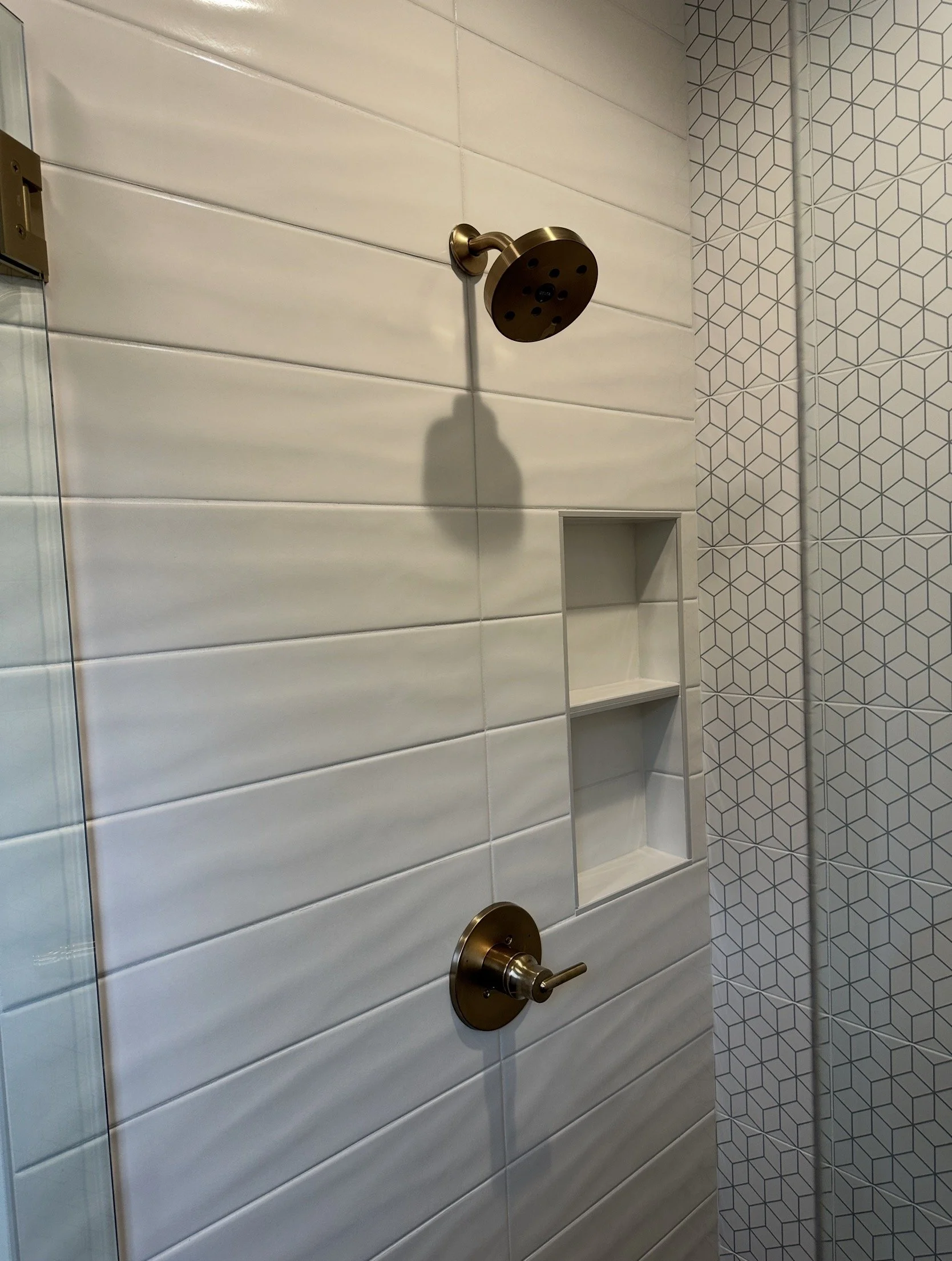 Bathroom shower with white tile wall, bronze showerhead, and built-in shelf.