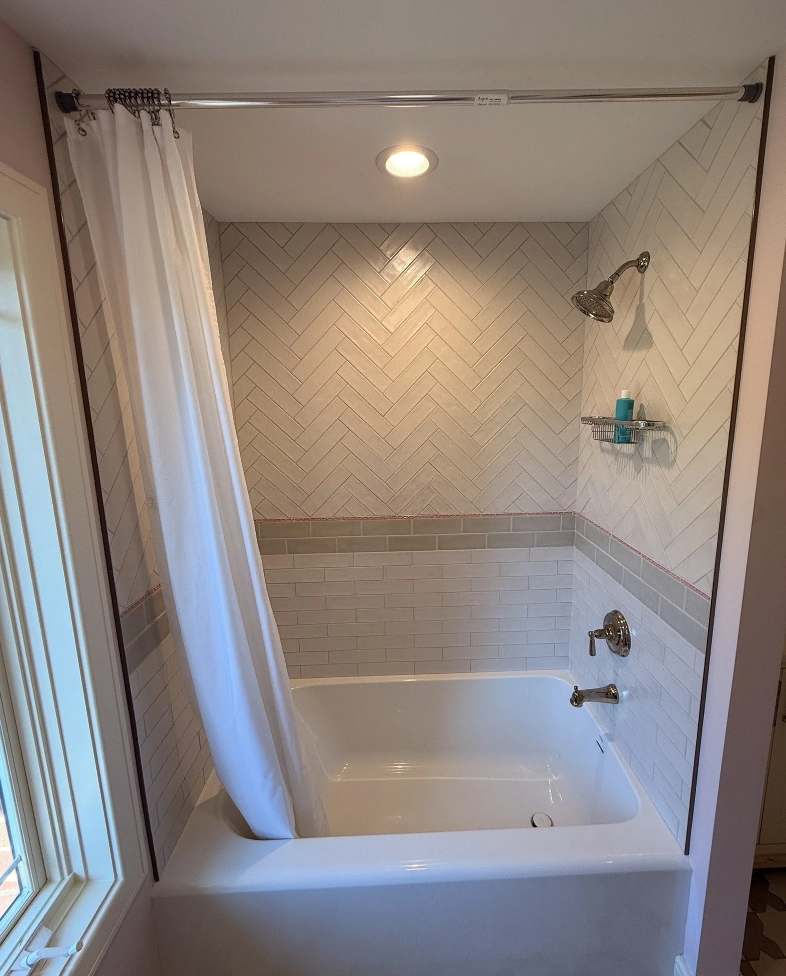 Bathroom shower with white curtain, tiled walls in beige and gray herringbone pattern, and a white bathtub.