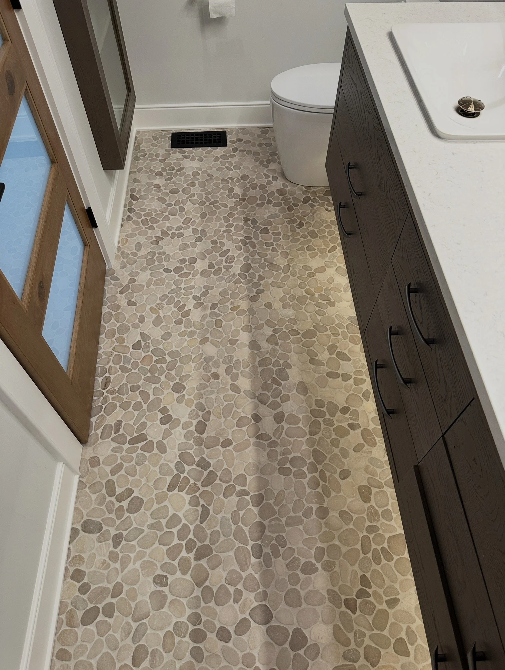 Bathroom with pebble tile flooring, white toilet, dark wood cabinet, and white countertop with an integrated sink.