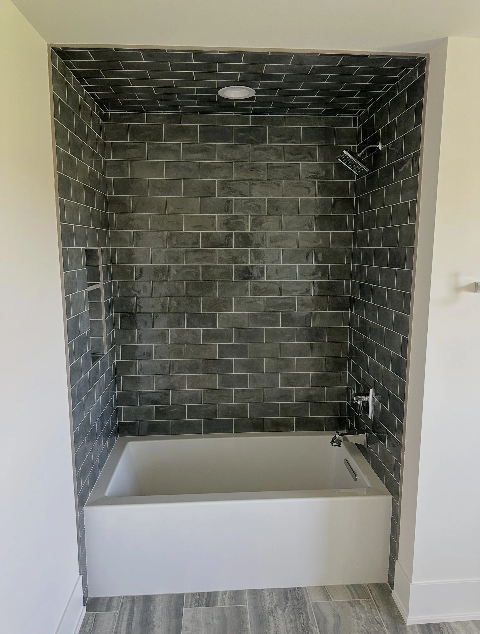 Bathroom shower area with dark gray brick tiles, a built-in niche, a ceiling light, a rain showerhead, and a bathtub.