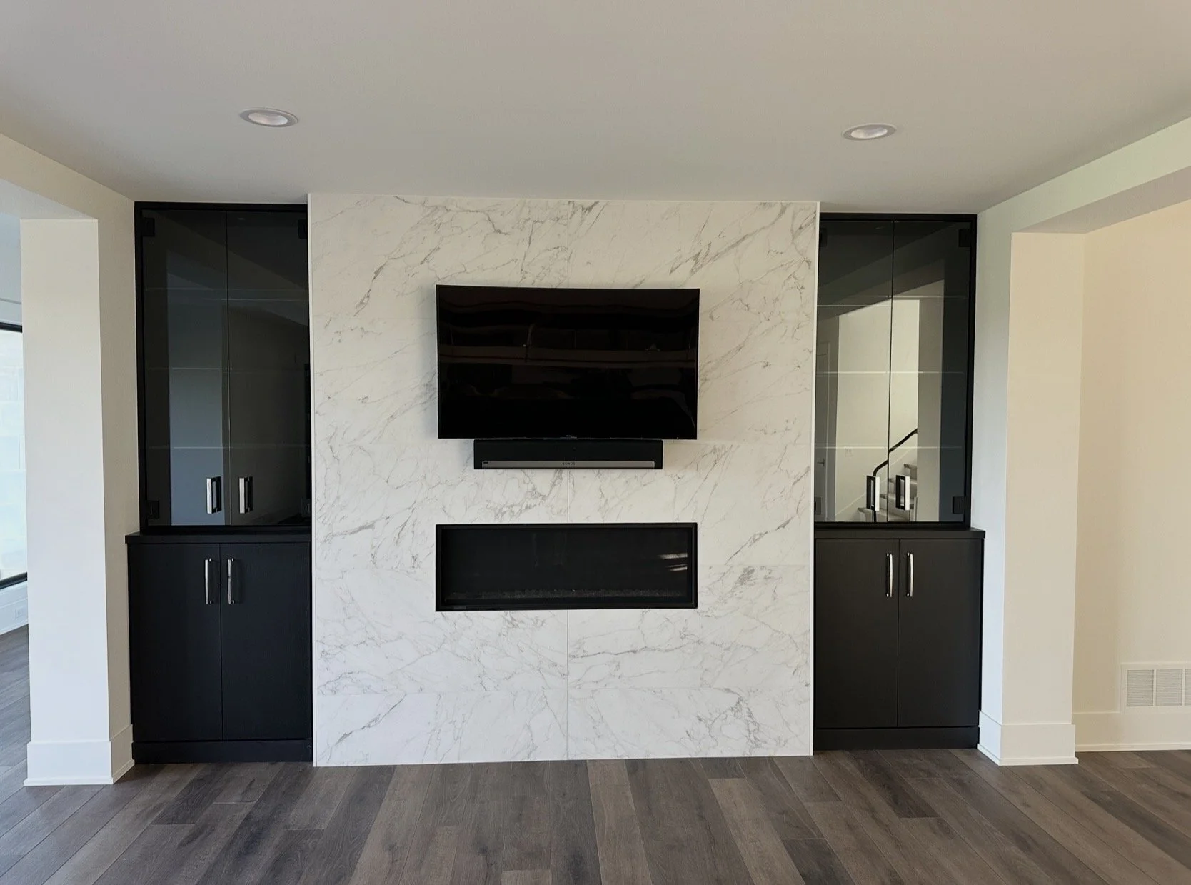 Modern living room with a white marble accent wall, mounted television, and black built-in cabinets with glass doors on either side.