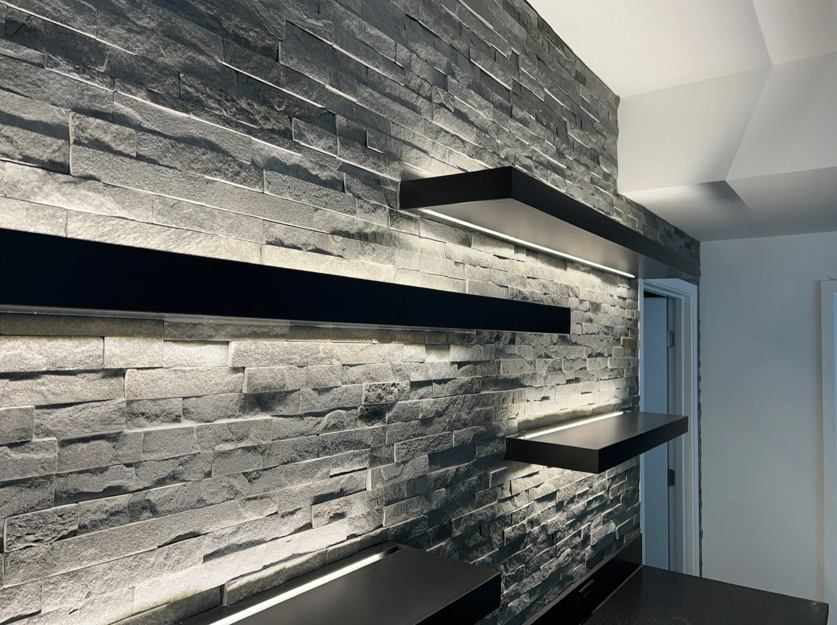 Interior view of a modern room featuring a gray stone accent wall with built-in black shelves and integrated lighting.