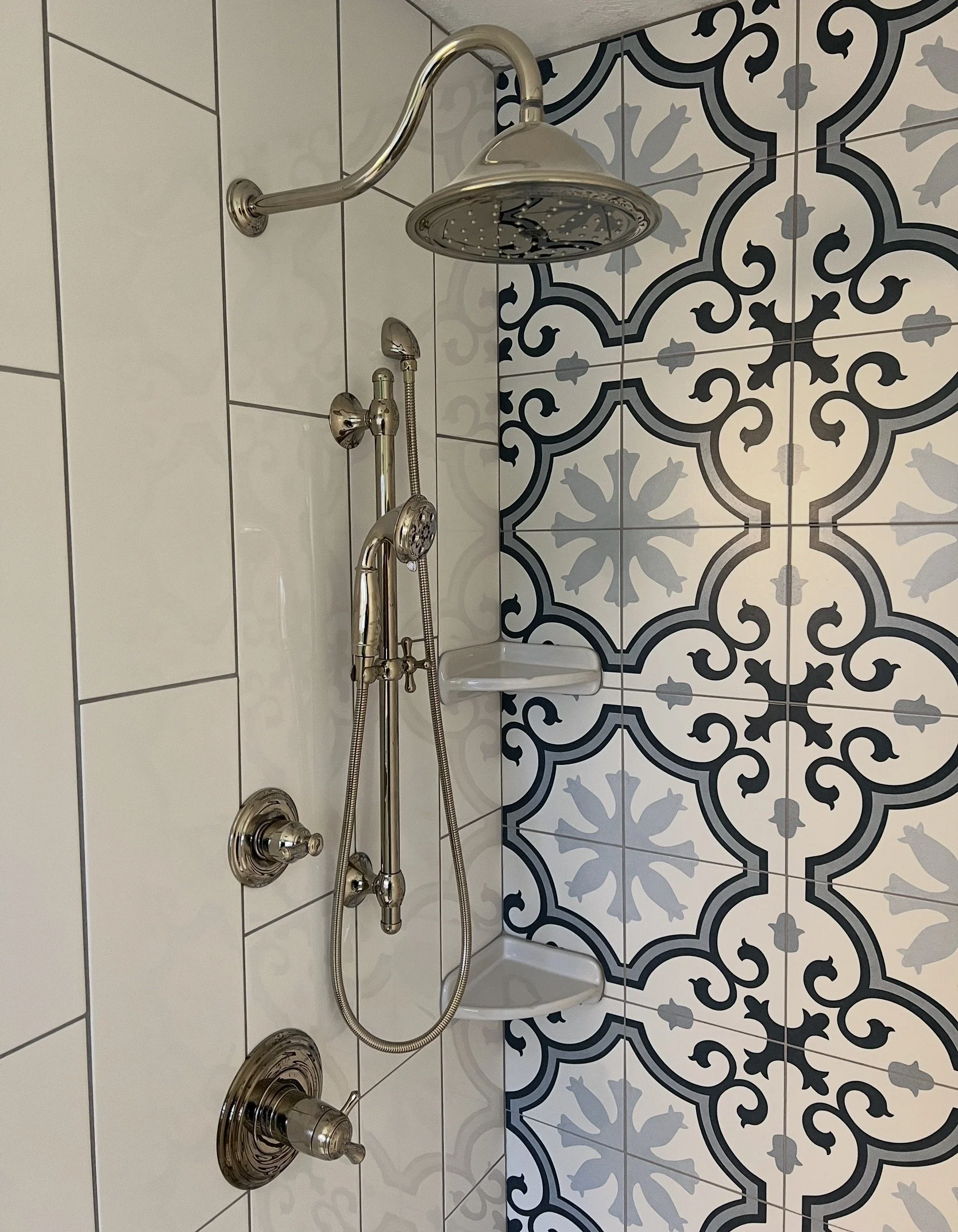 Shower area featuring a chrome showerhead, a handheld shower attachment, and a soap dish mounted on the wall, with a decorative black and white patterned tile wall in the background.