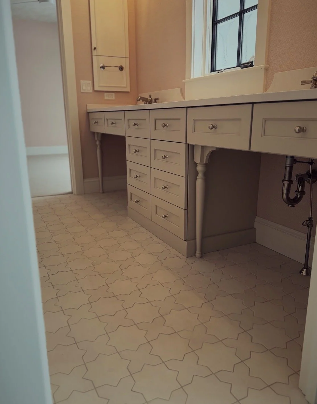 Empty bathroom vanity with a mirror and a window, beige walls, white cabinets, and beige patterned tile floor.