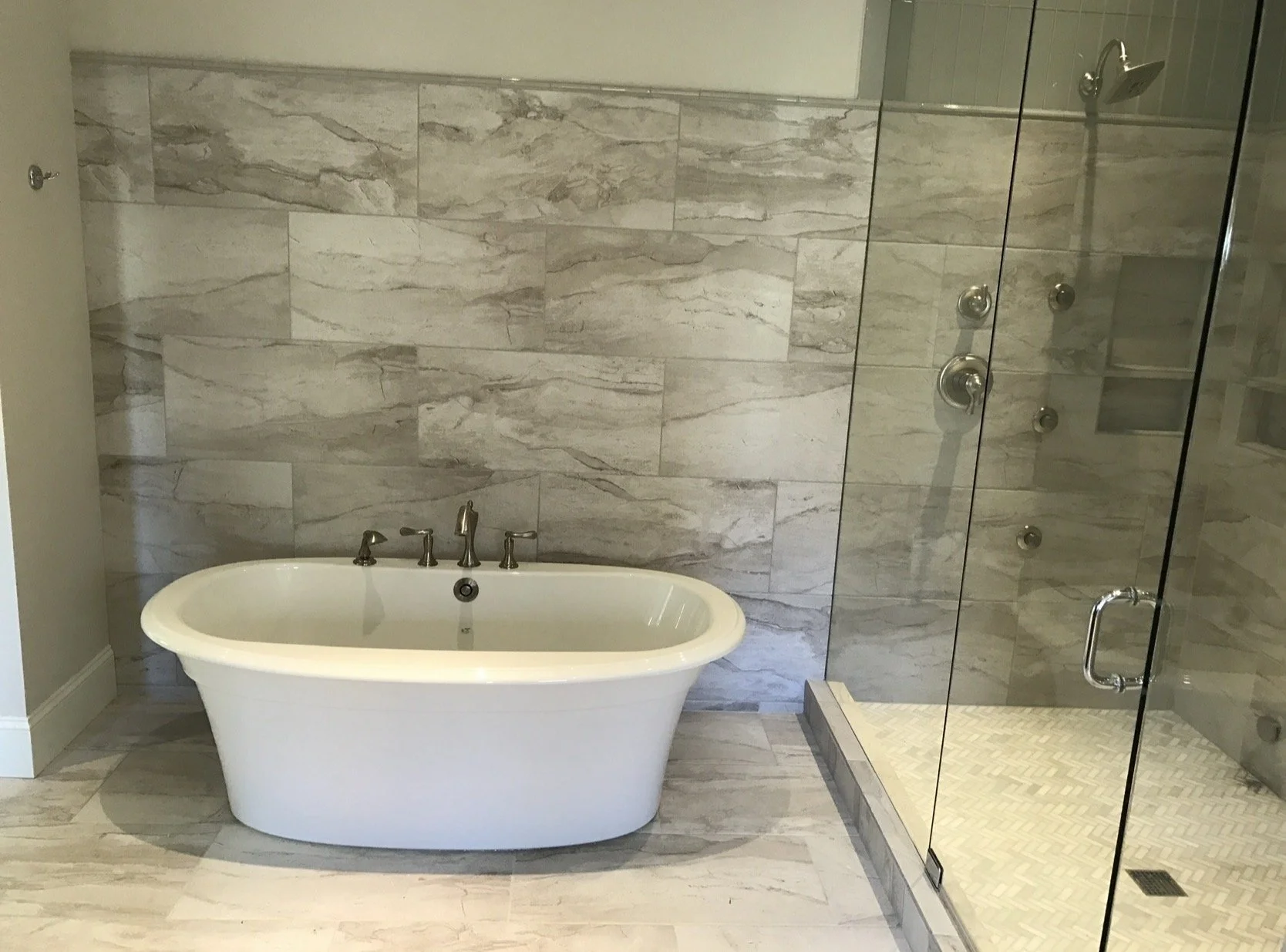 Bathroom with free-standing bathtub, marble walls, and a glass shower enclosure with multiple shower heads.