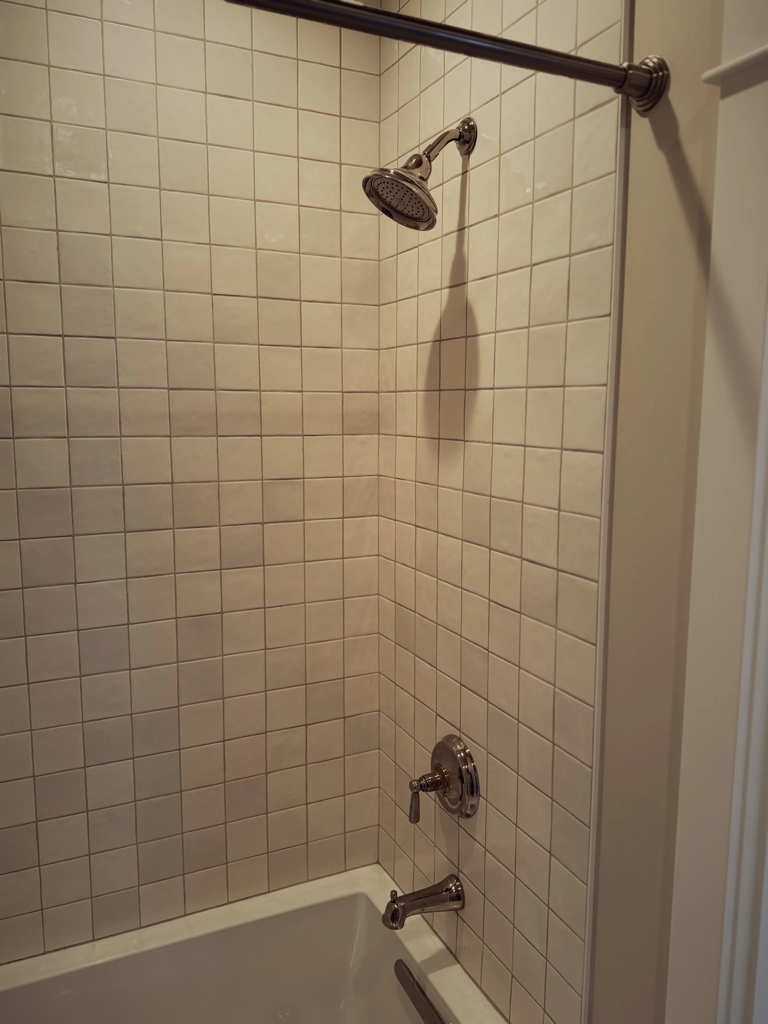 Bathroom shower with beige tiled walls, a chrome showerhead, and a chrome faucet and handle.
