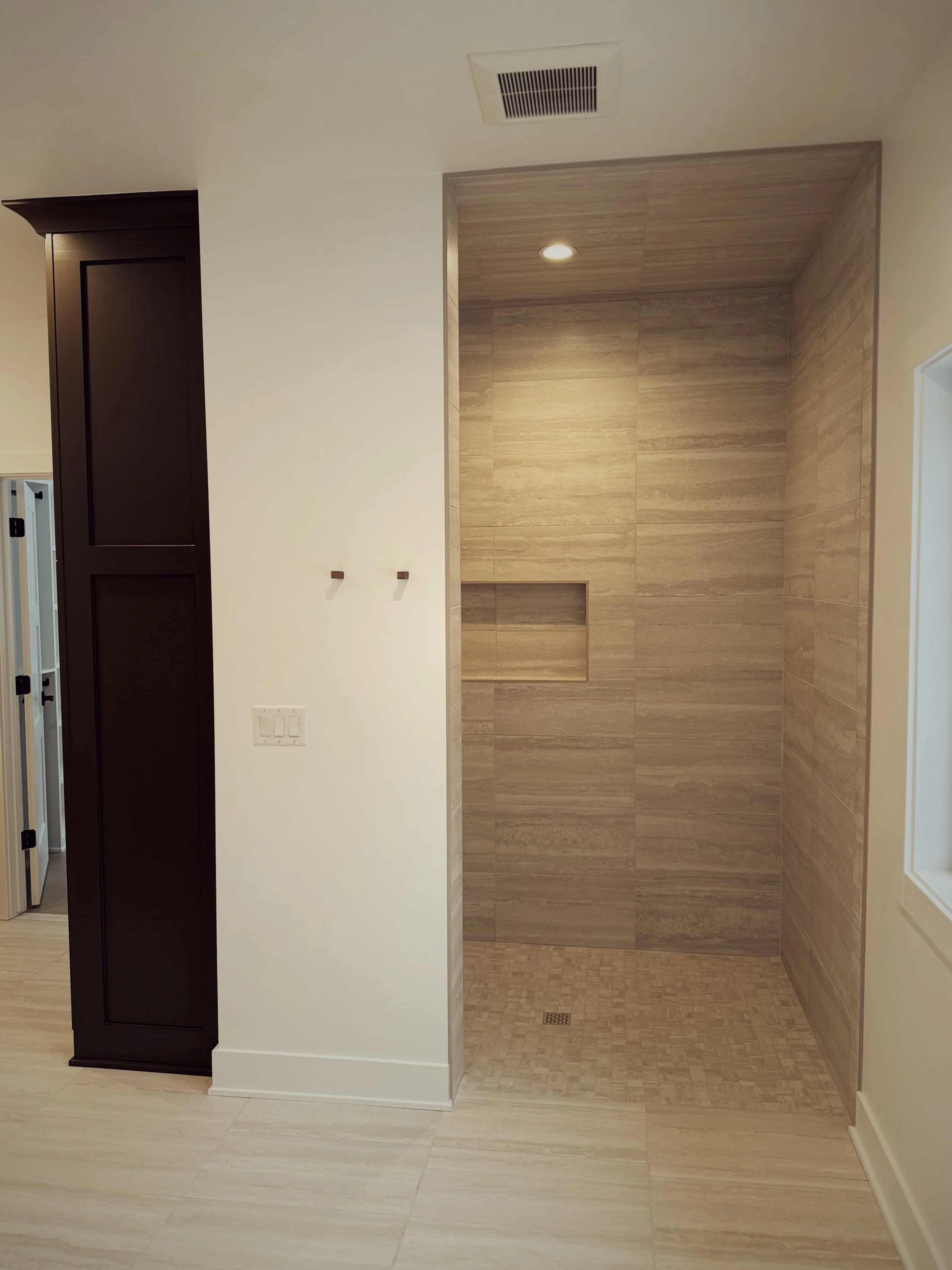 Empty walk-in shower with wooden-look tiles, built-in niche, and ceiling light, in a modern bathroom.