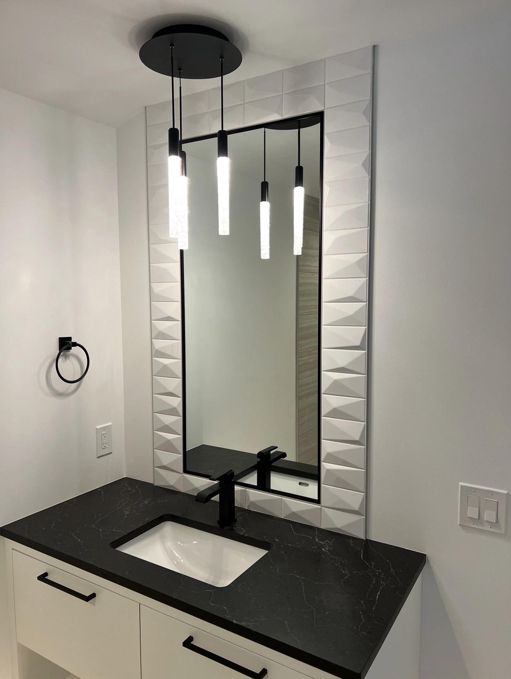 Modern bathroom vanity with black countertop, white sink, large mirror, and hanging pendant lights.