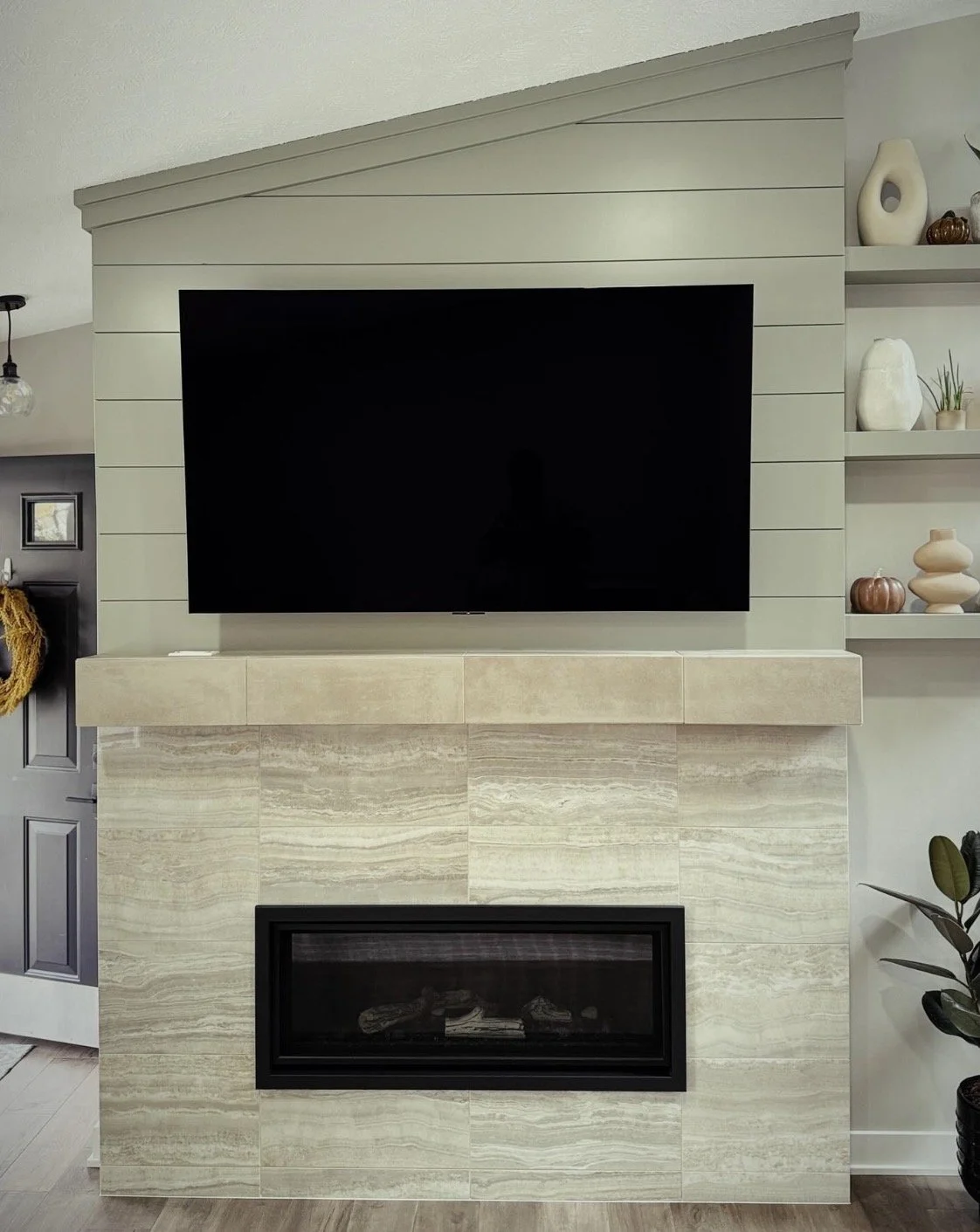 Living room fireplace with a mounted flat-screen TV above it, decorated with vases and natural decor on the wall shelves.