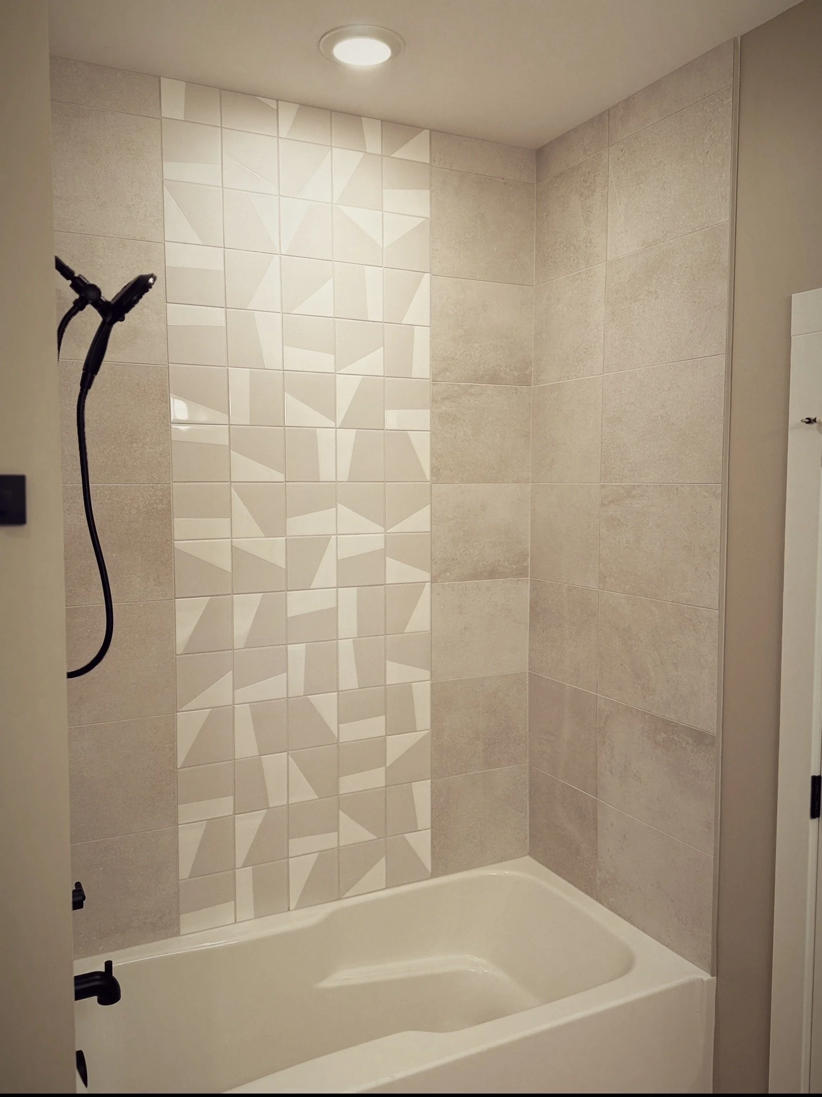 A bathtub with beige and patterned wall tiles and a black showerhead.