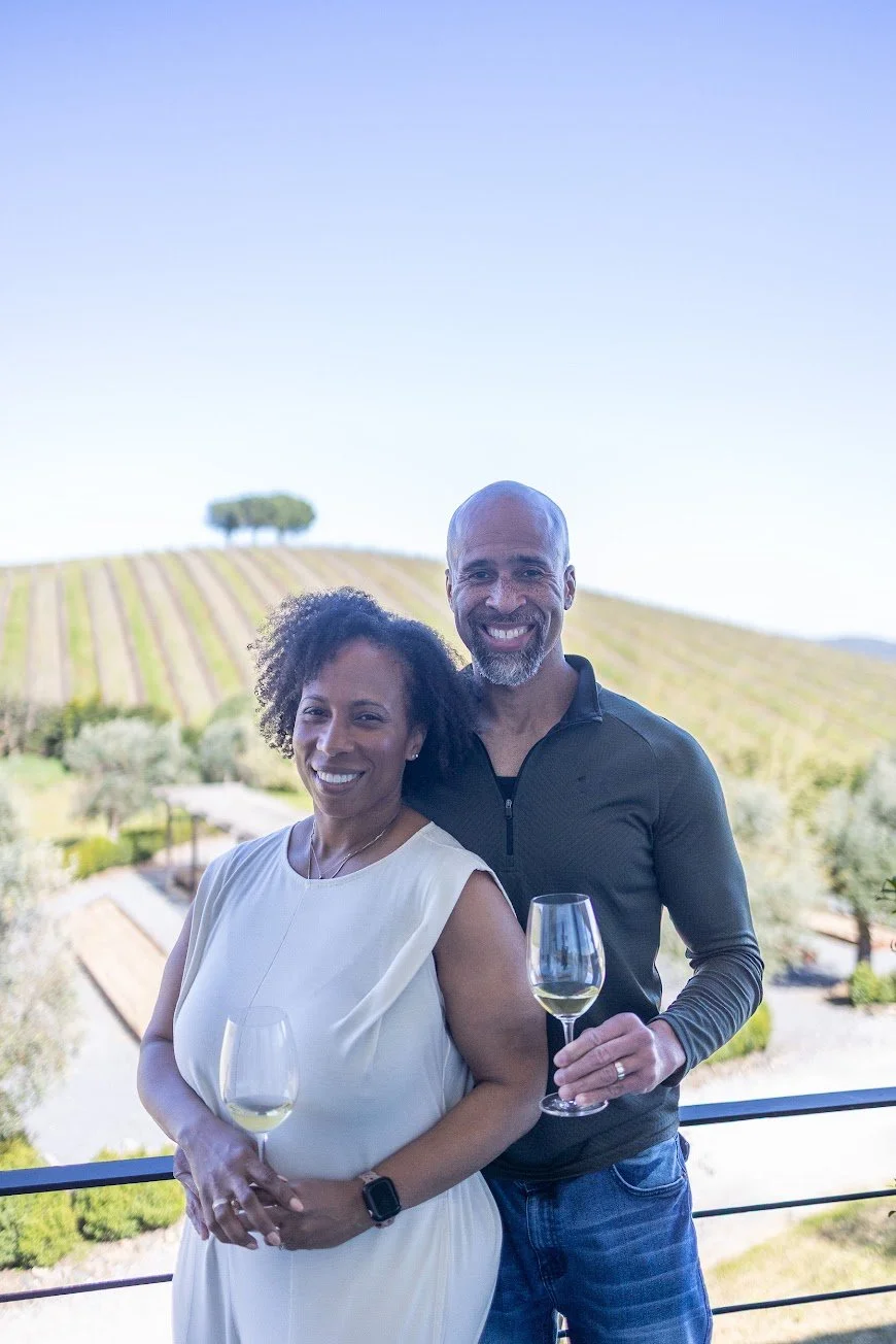 couple standing in front of vineyards with a glass of wine