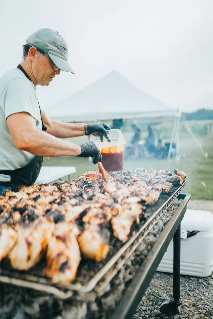 Man grilling barbecue chicken alongside vineyards