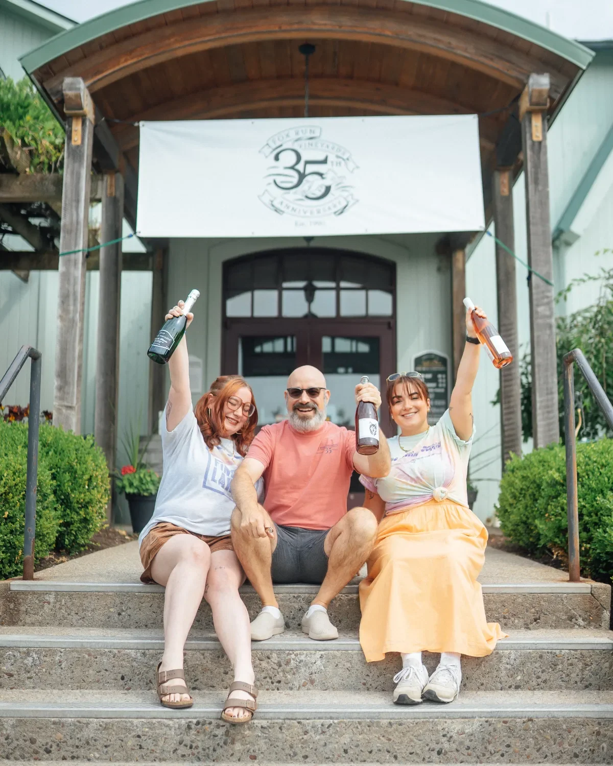 three smiling employees holding up Fox Run wine bottles at the entrance