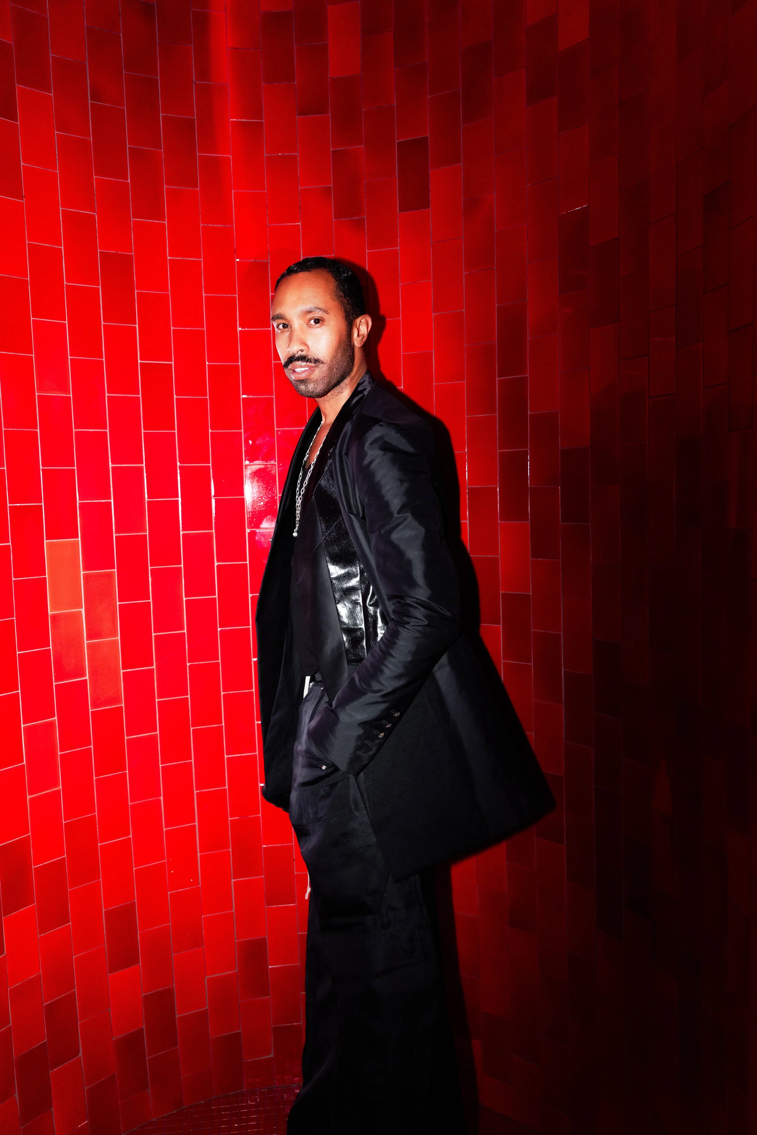 Man in black jacket standing against a red tiled wall.