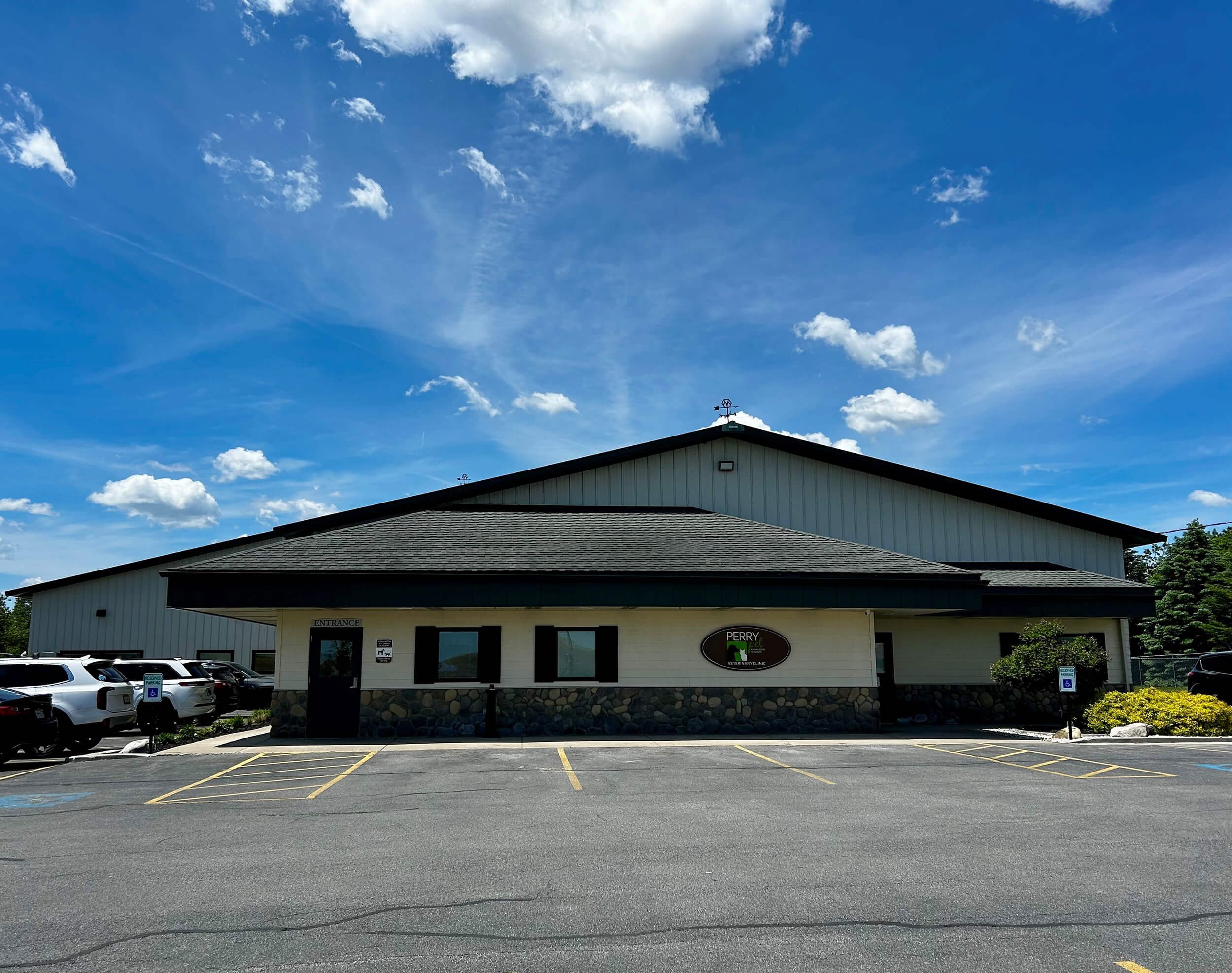 Building with a sign for Perry Vet, a veterinary clinic, with a parking lot in front and a few cars parked. The sky is blue with scattered clouds.