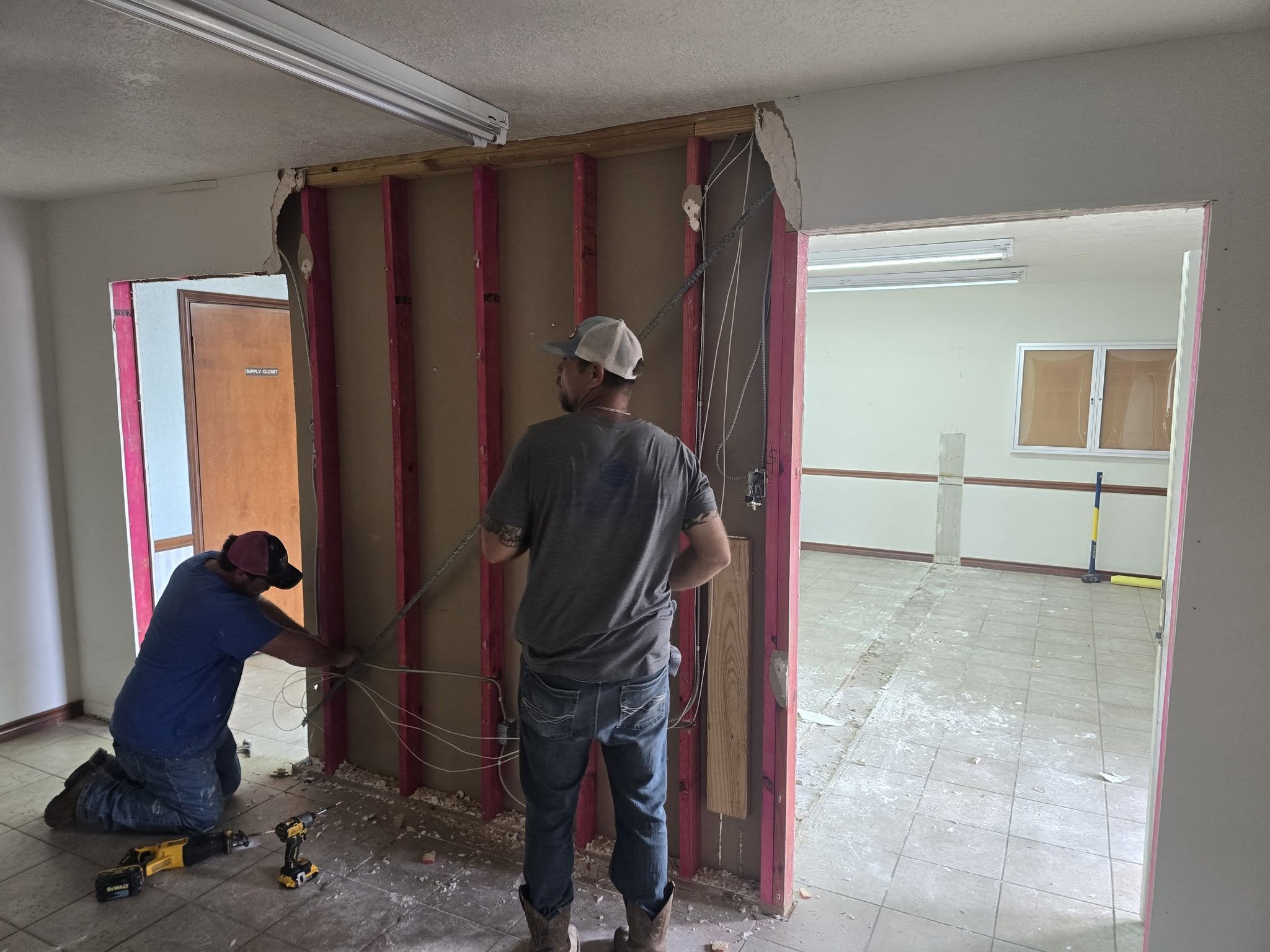 Two workers constructing a wall with pink insulation and wood framing inside a building under renovation.