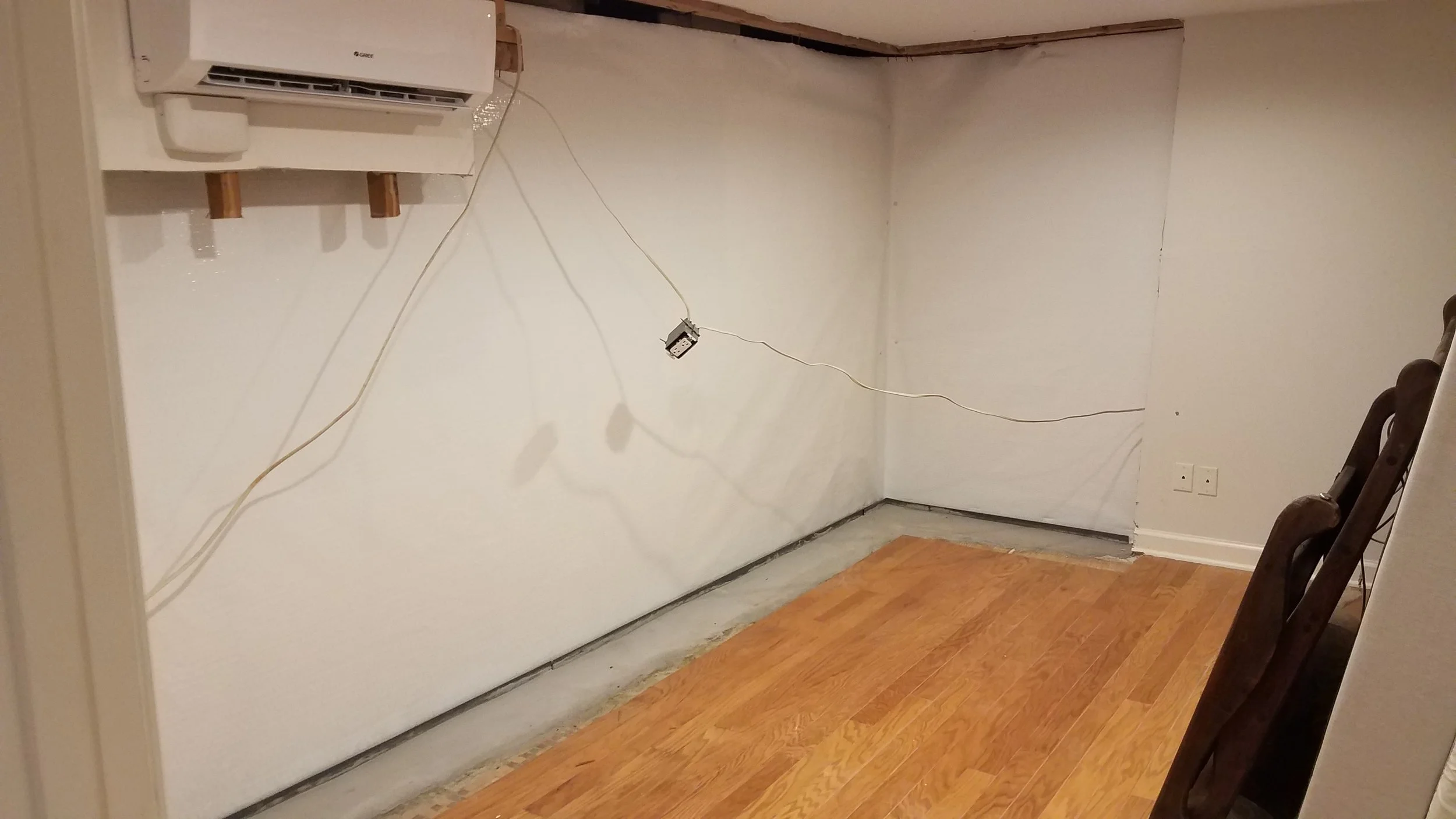 Empty room with partially installed closet or wall cabinet, wires hanging from the wall, and a chair in the corner.