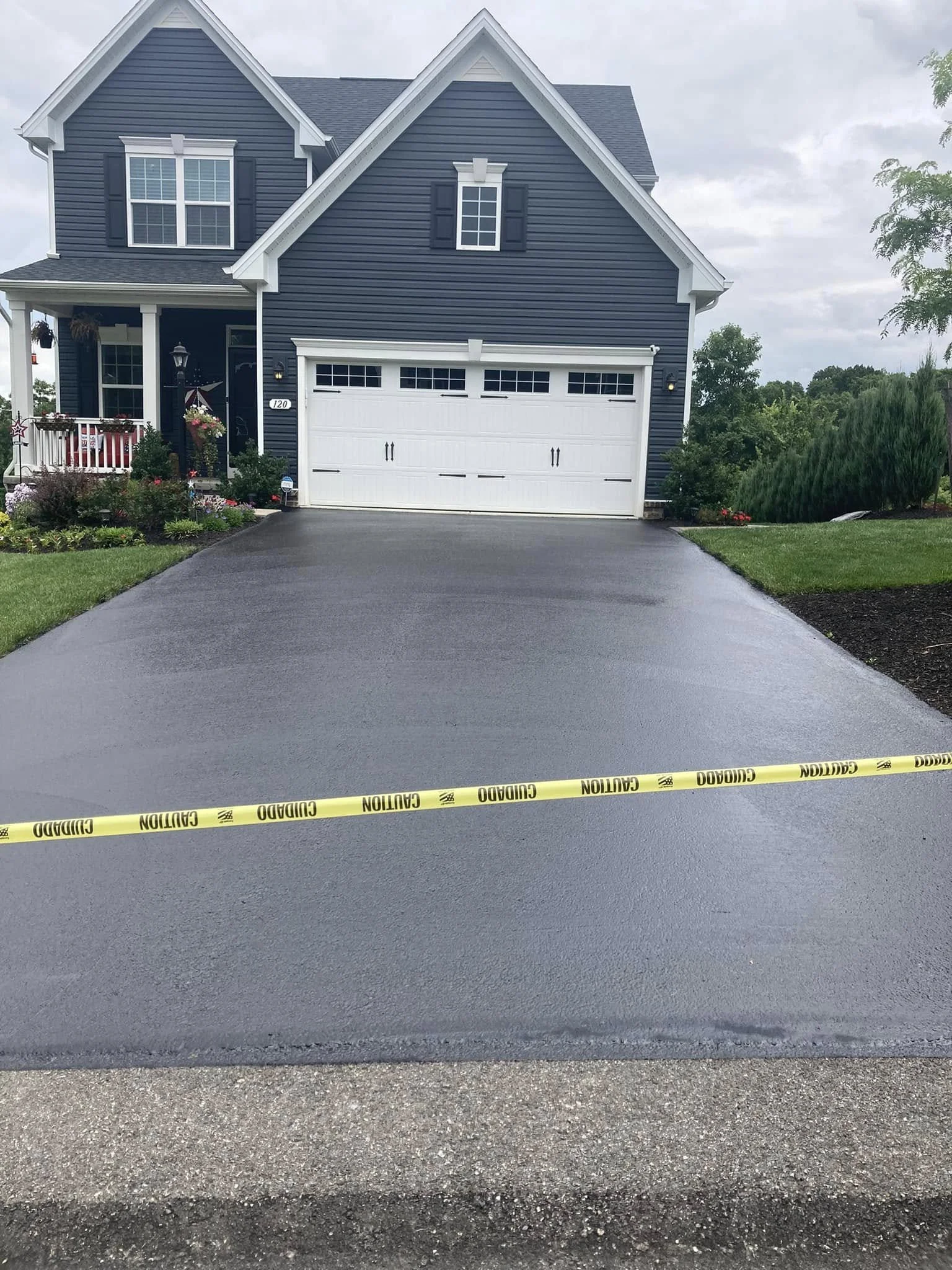 Newly paved driveway in front of blue house with white garage door, decorated front porch, and lush green lawn.