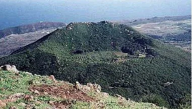 Un vulcano verde con vegetazione circondato da un paesaggio arido.