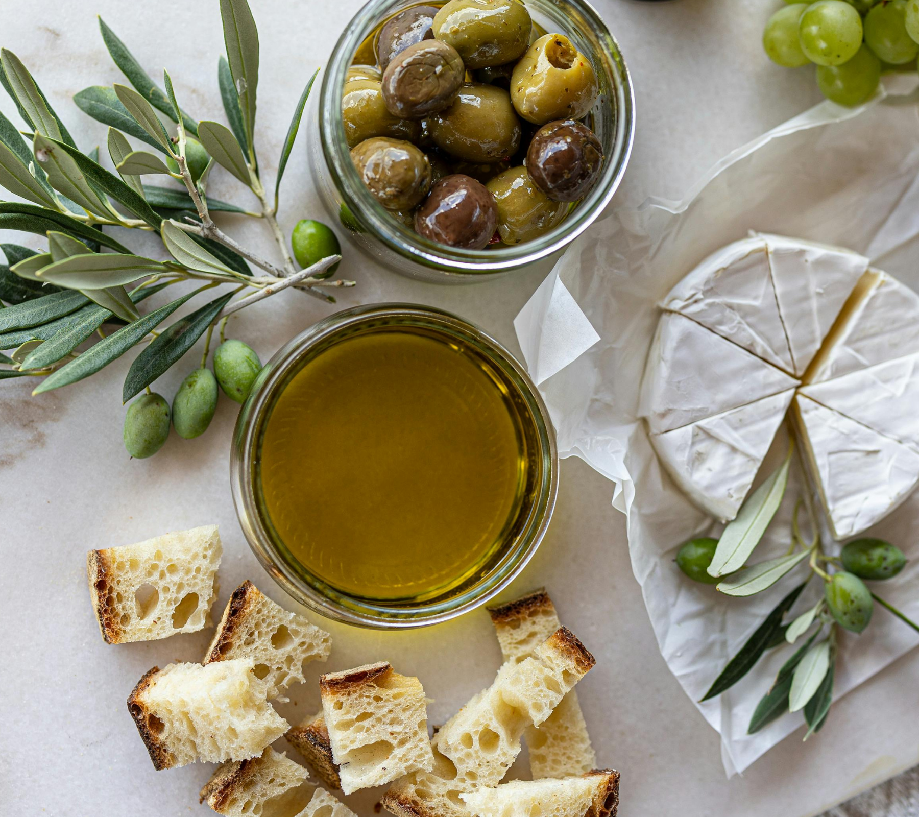 A charcuterie display of cheeses, breads, olives, and a bowl of olive oil