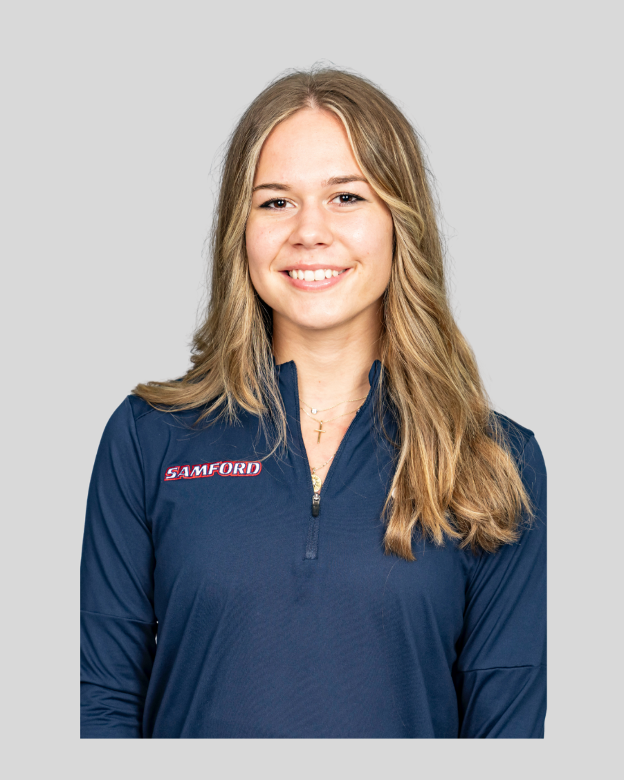 A young woman with long blonde hair, smiling, wearing a dark blue athletic jacket with a 'SAMFORD' logo on the chest, against a light gray background.