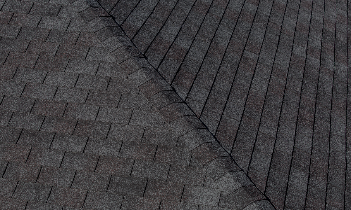Close-up of a roof with dark asphalt shingles arranged in a pattern, showing the edge of a section overlapping another.