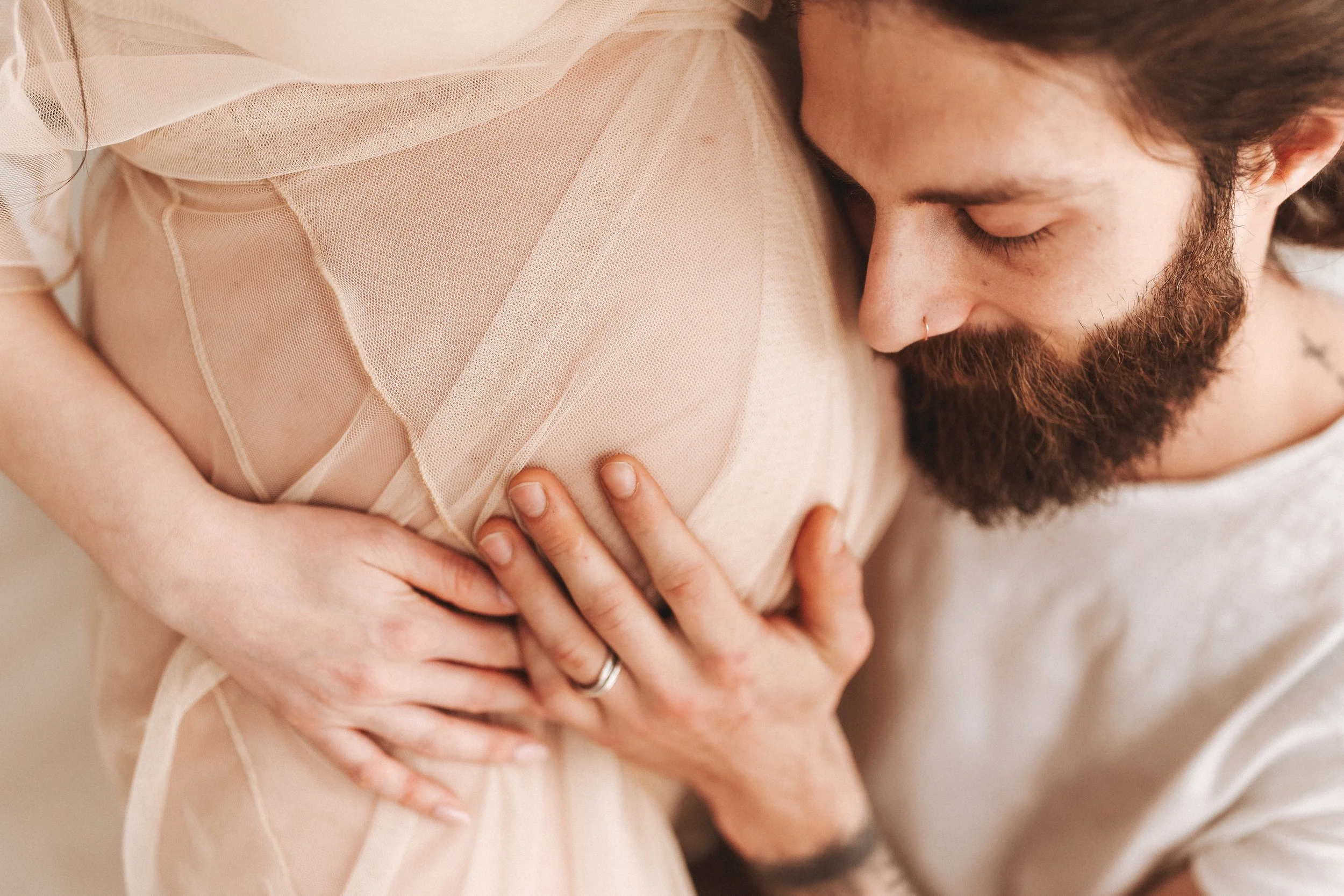 Servizio fotografico gravidanza a Prato, futura mamma abbracciata dal partner con mano sulla pancia in studio.