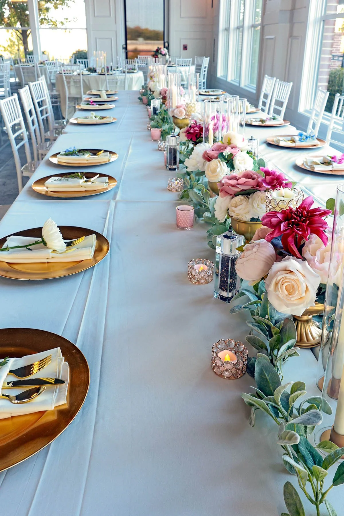 Silk floral arrangements, candlelight and gold table accents across a wedding reception table