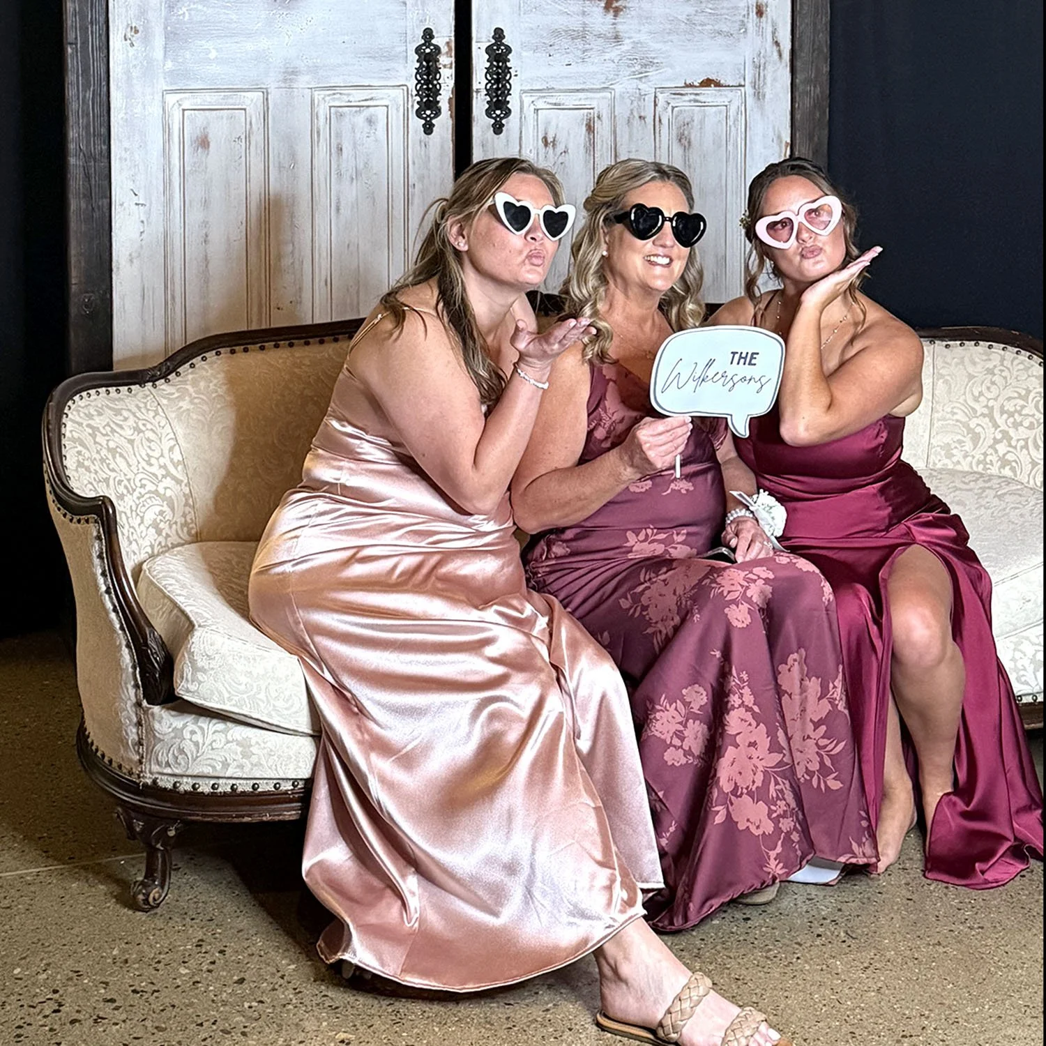Three wedding guests sharing a playful portrait on a styled vintage sofa