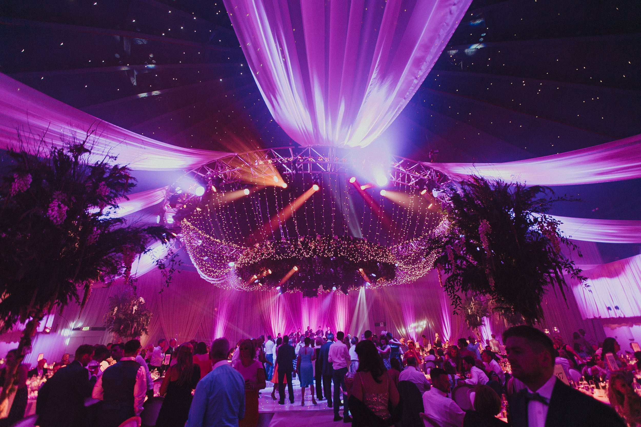 Around the edges, candlelit tables and elegant chairs frame the scene, making the whole setting feel like an immersive evening in a magical, twilight ballroom.