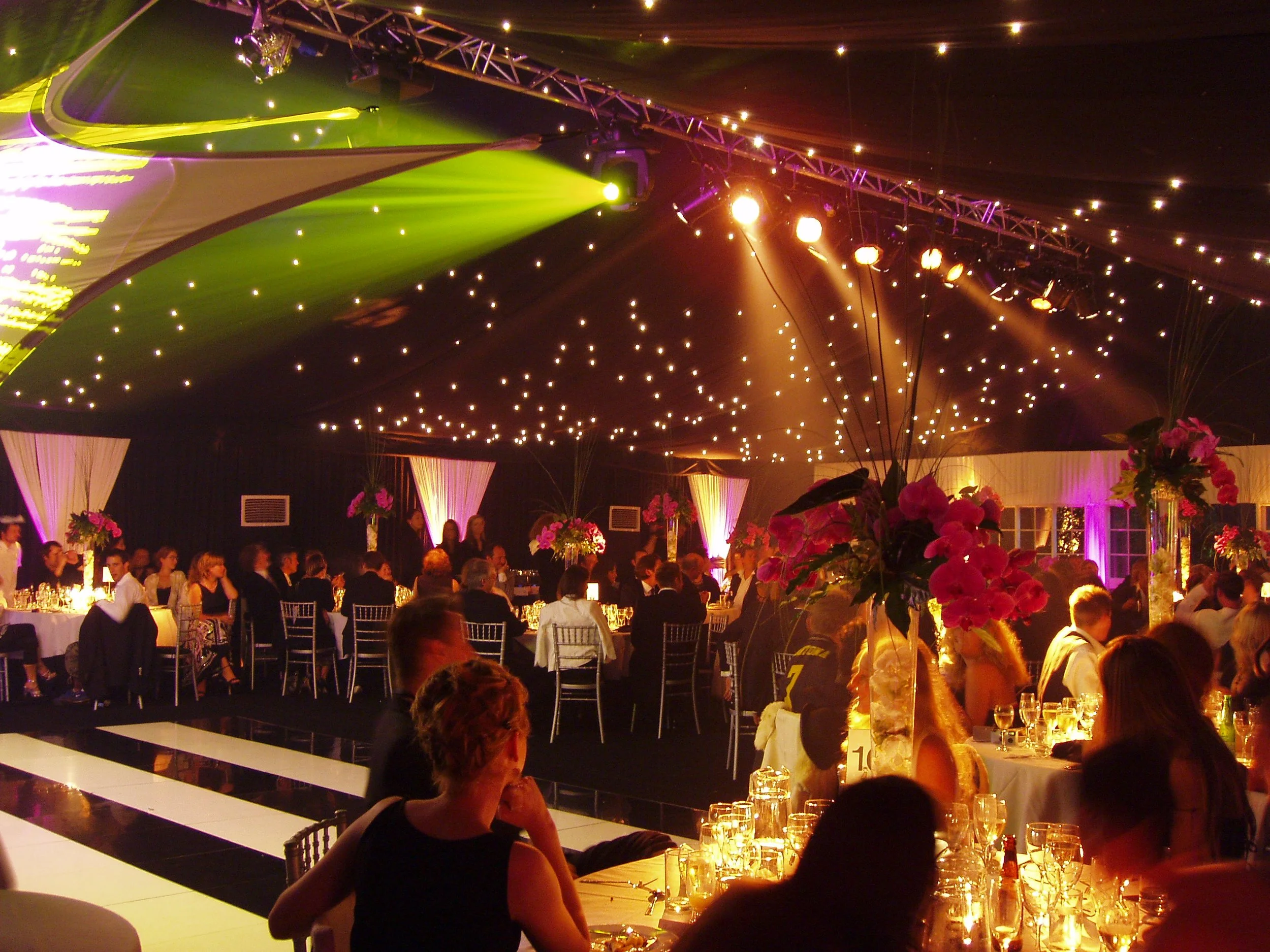 A large banquet hall decorated with pink flowers and elegant lighting, filled with guests seated at tables for a formal event or celebration.
