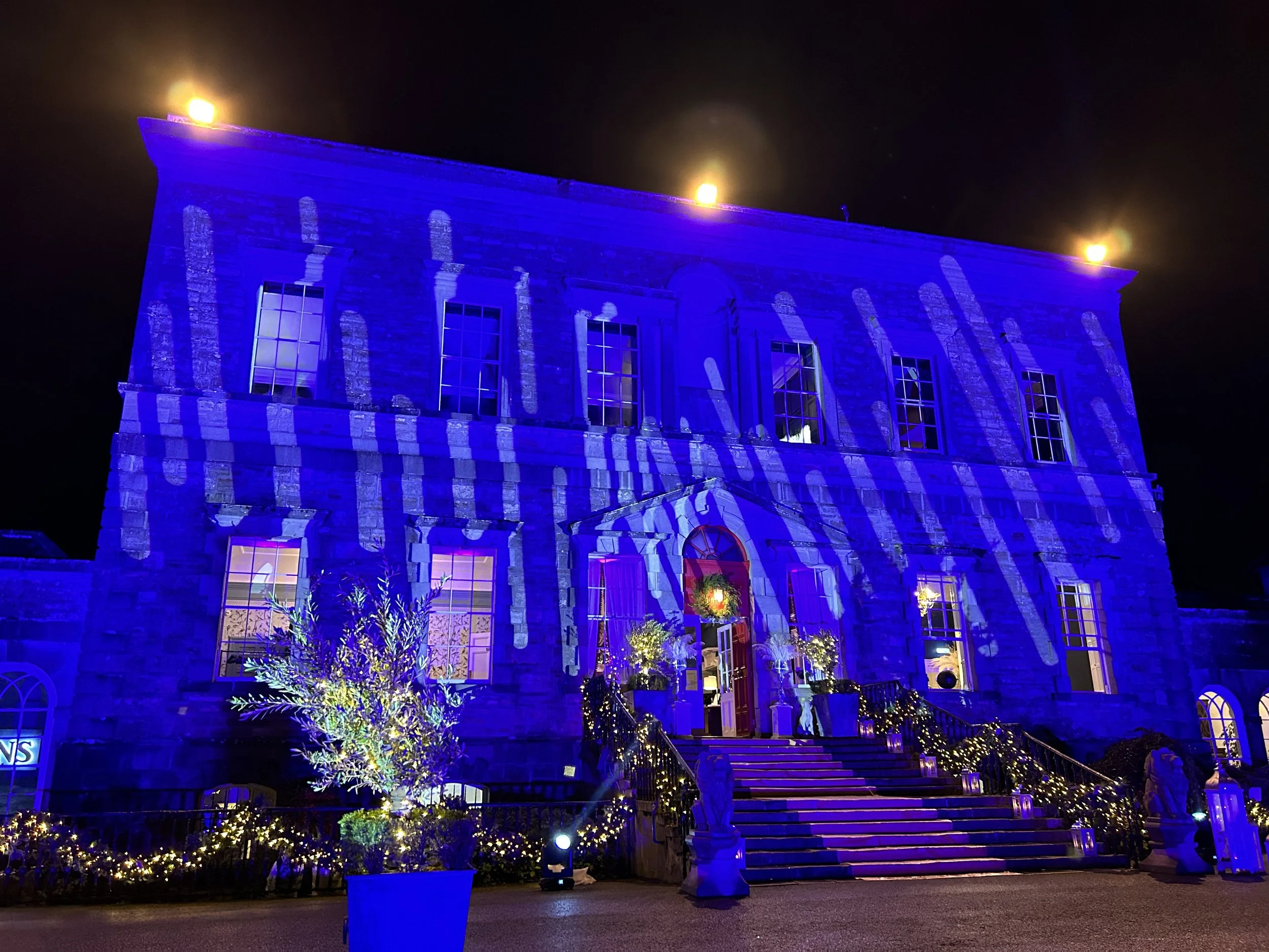 The entire façade is washed in vivid blue light, with textured patterns projected onto the stone to create movement and depth, making the architecture feel almost theatrical.