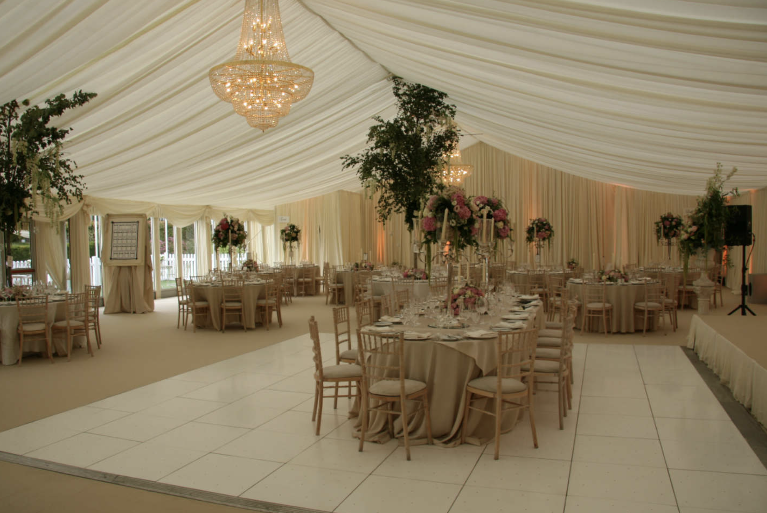 Elegant event tent decorated with chandeliers, floral centerpieces, and arranged dining tables for a celebration.