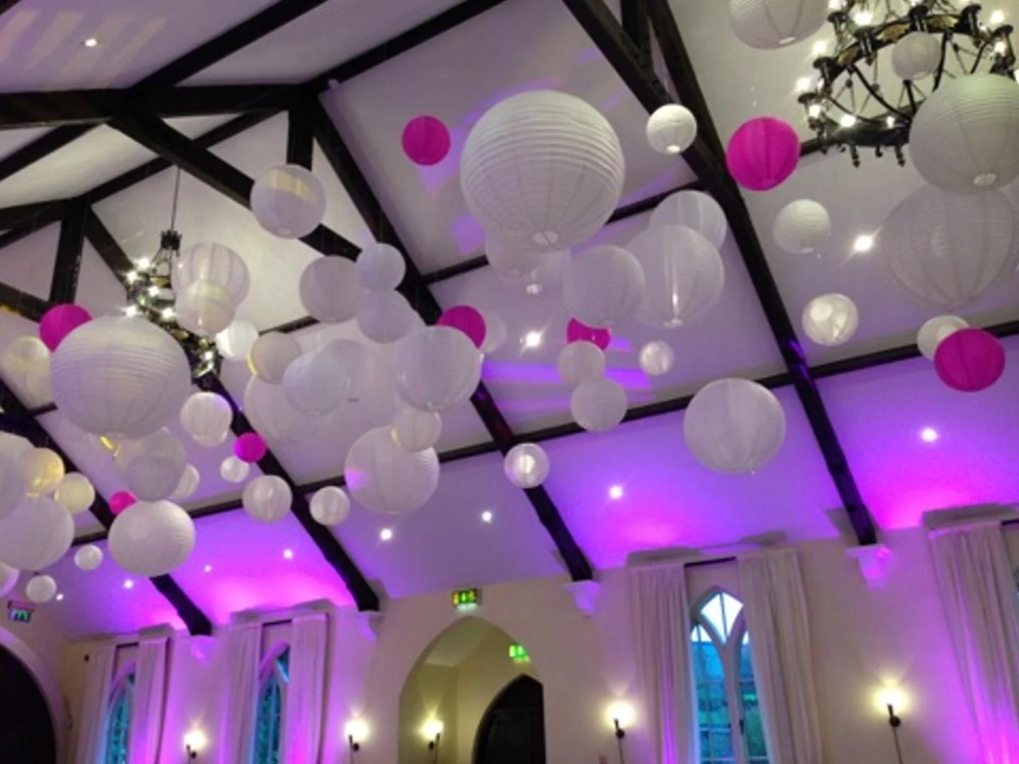Ceiling decorated with hanging white and pink paper lanterns, with purple lighting and a chandelier.