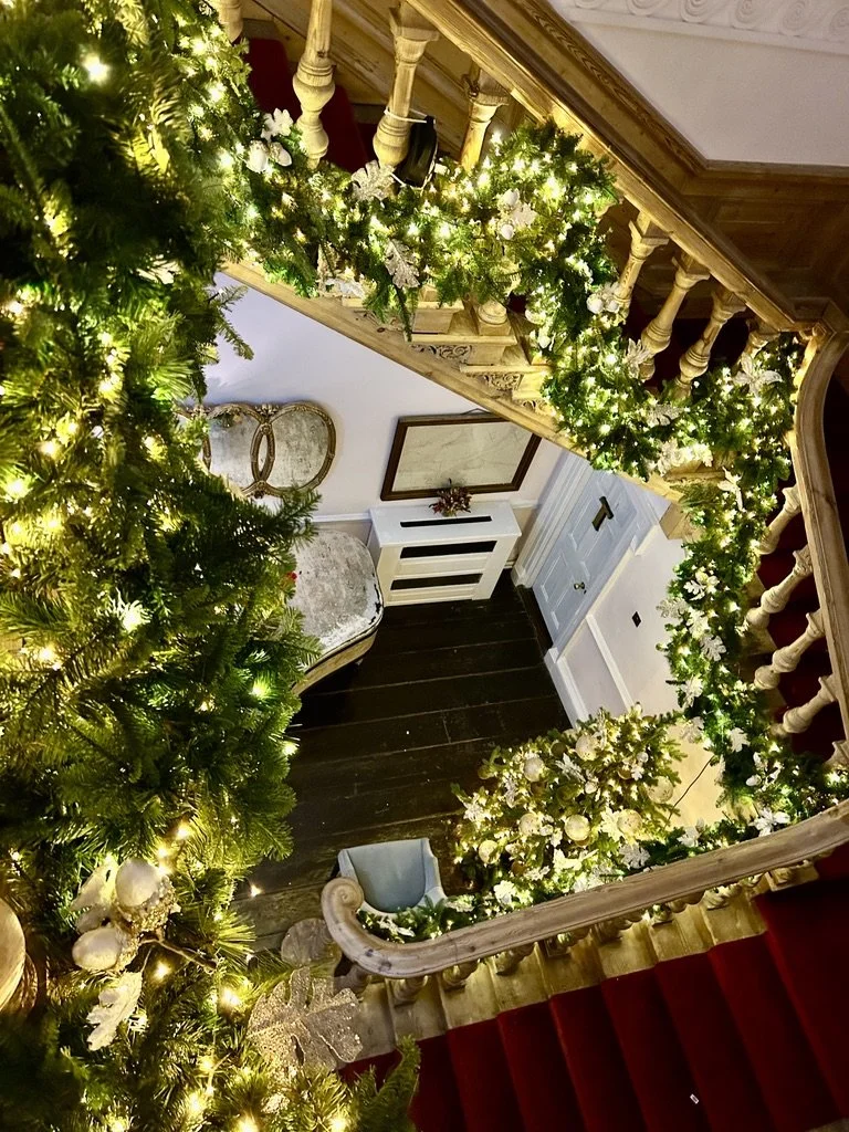 Decorated staircase with Christmas garland and lights, a Christmas tree visible on the left, and a small sofa at the bottom of the stairs.
